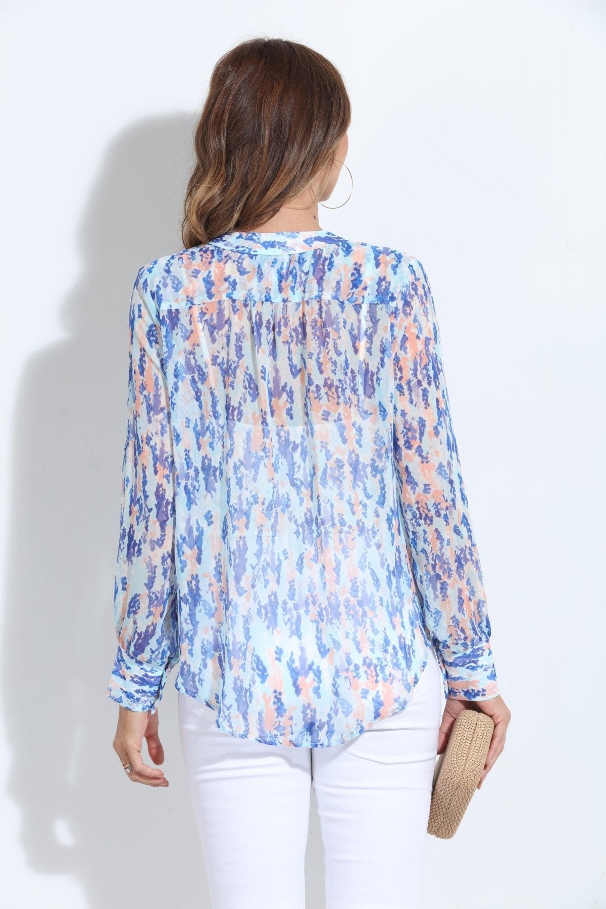 backside of multi-colored, long sleeve blouse on woman in white pants and holding tan purse