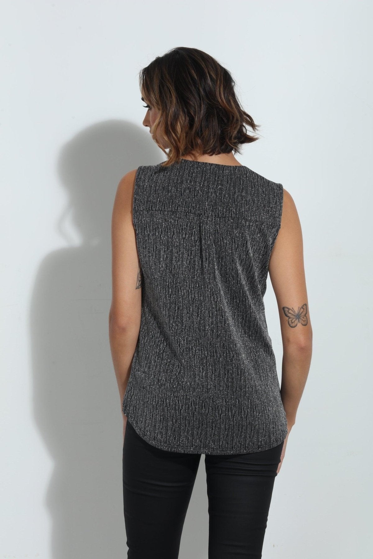 back side of silver sparkle sleeveless blouse on woman in black pants