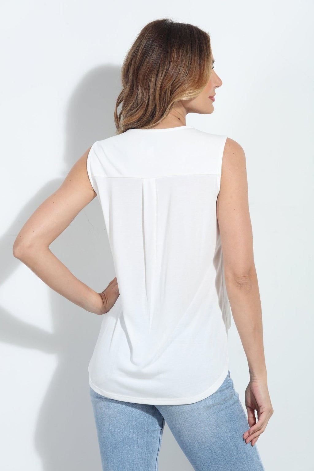 backside of ivory sleeveless blouse on woman in denim pants