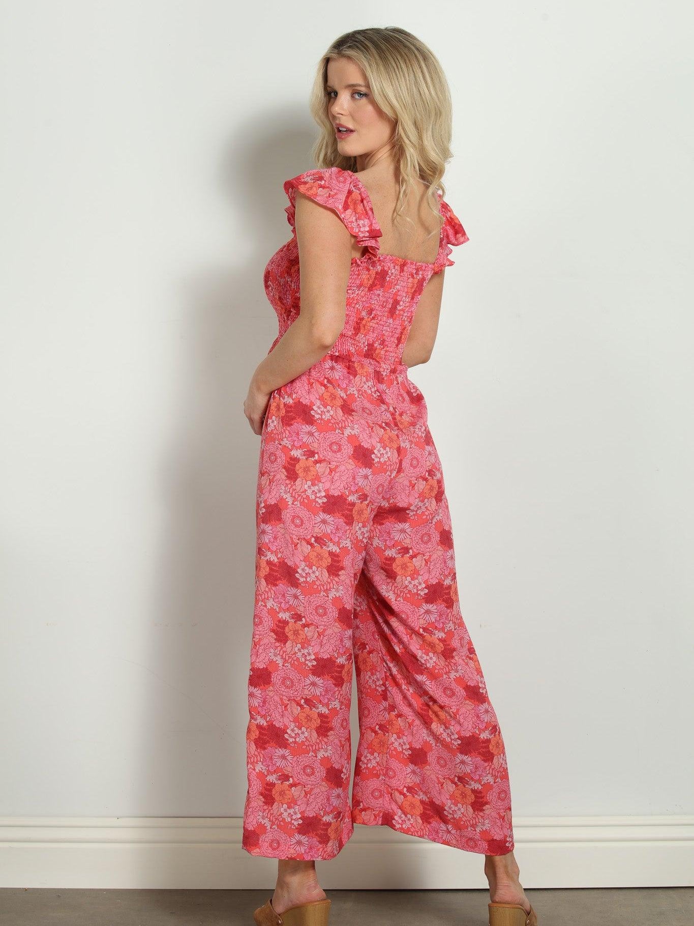 back side of pink and red floral sleeveless jumpsuit styled on woman wearing tan high heels