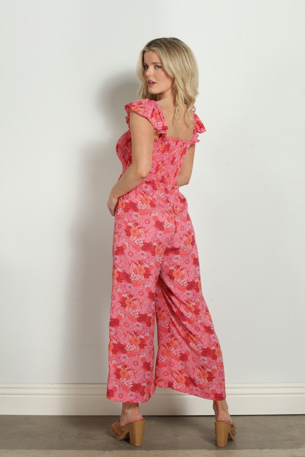 back side of pink and red floral sleeveless jumpsuit styled on woman wearing tan high heels