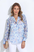 multi-colored, long sleeve blouse on woman in white pants and holding tan purse