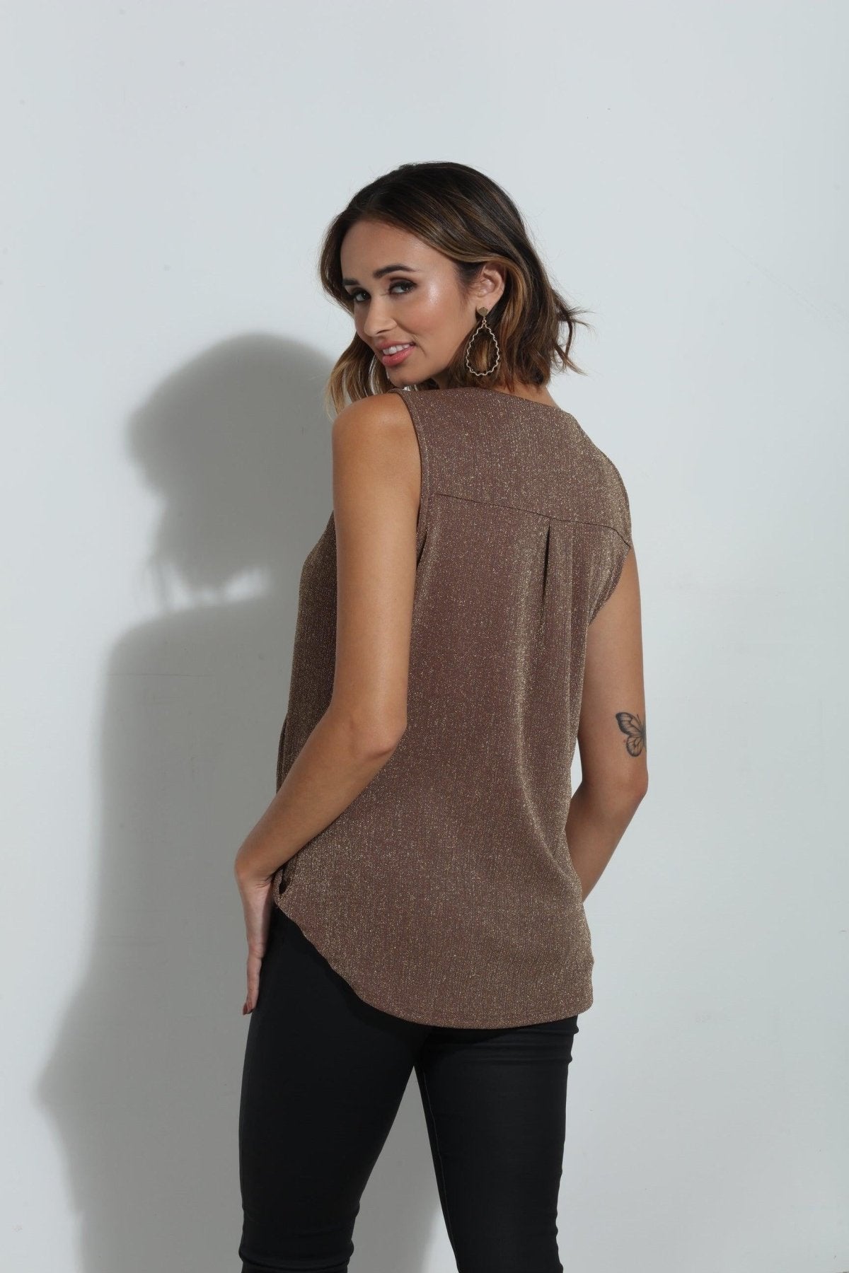 back side of brown sparkle sleeveless blouse on woman in black pants