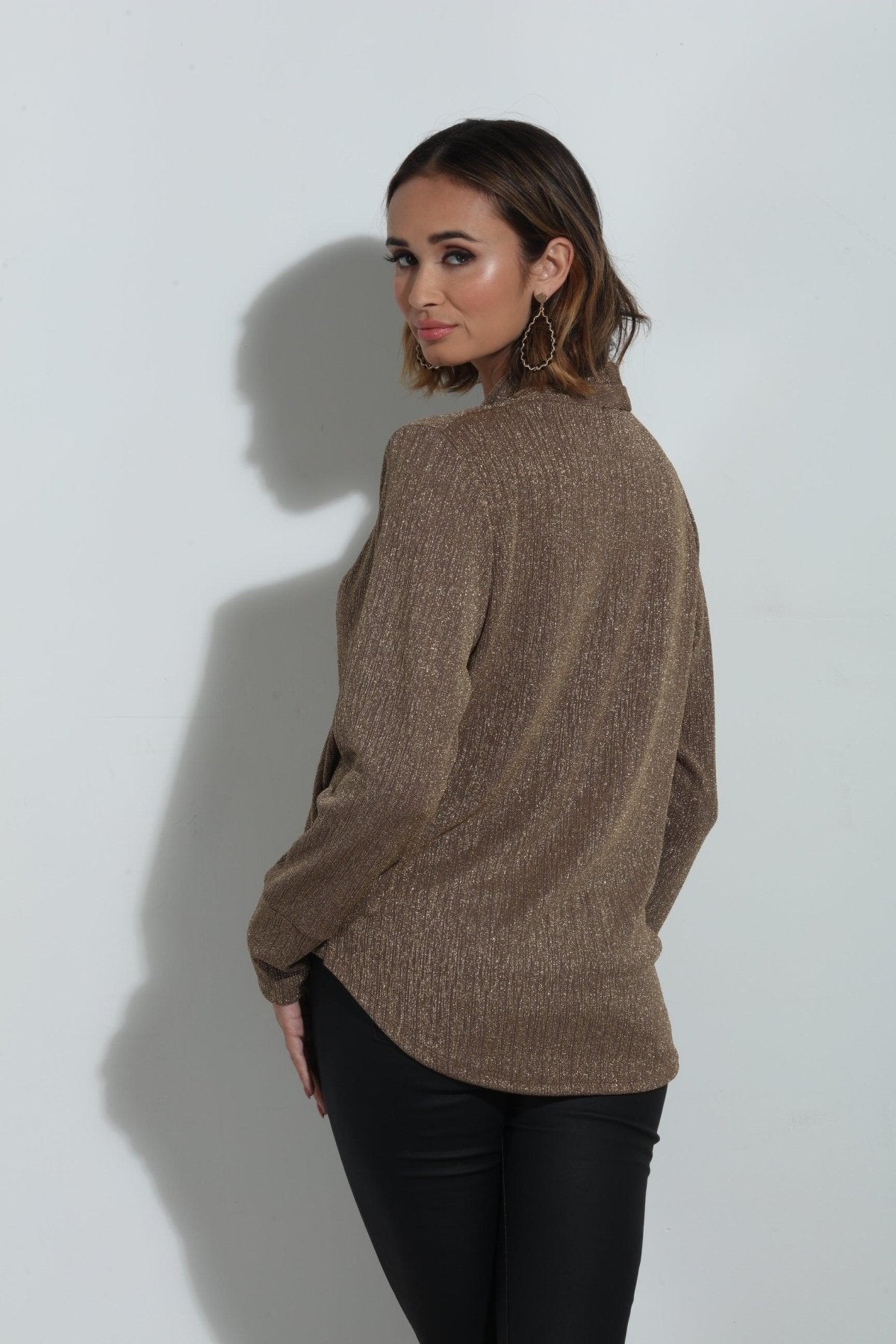 back side of brown sparkle long sleeve blouse on woman in black pants