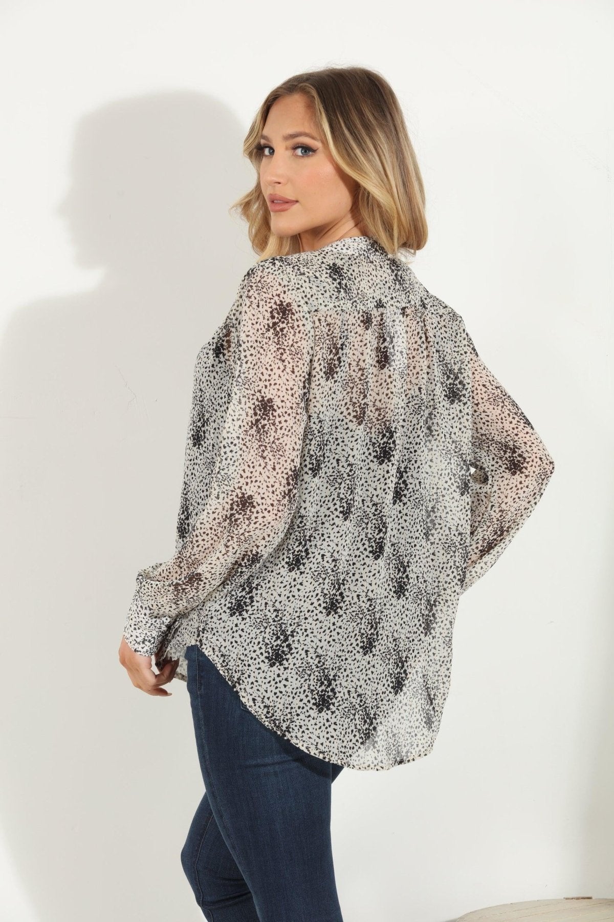 back side of white and black printed long sleeve blouse on woman in denim pants