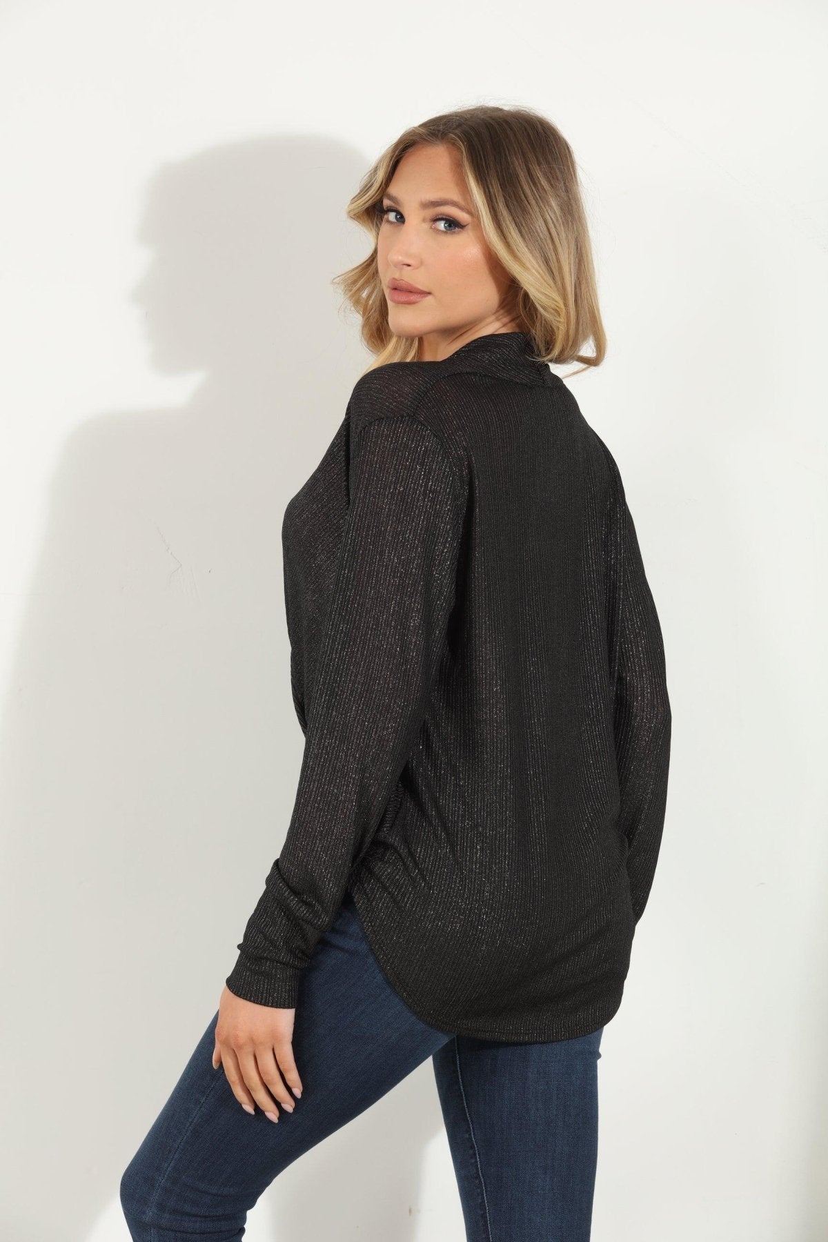 backside of black and sparkle long sleeve blouse on woman in denim pants