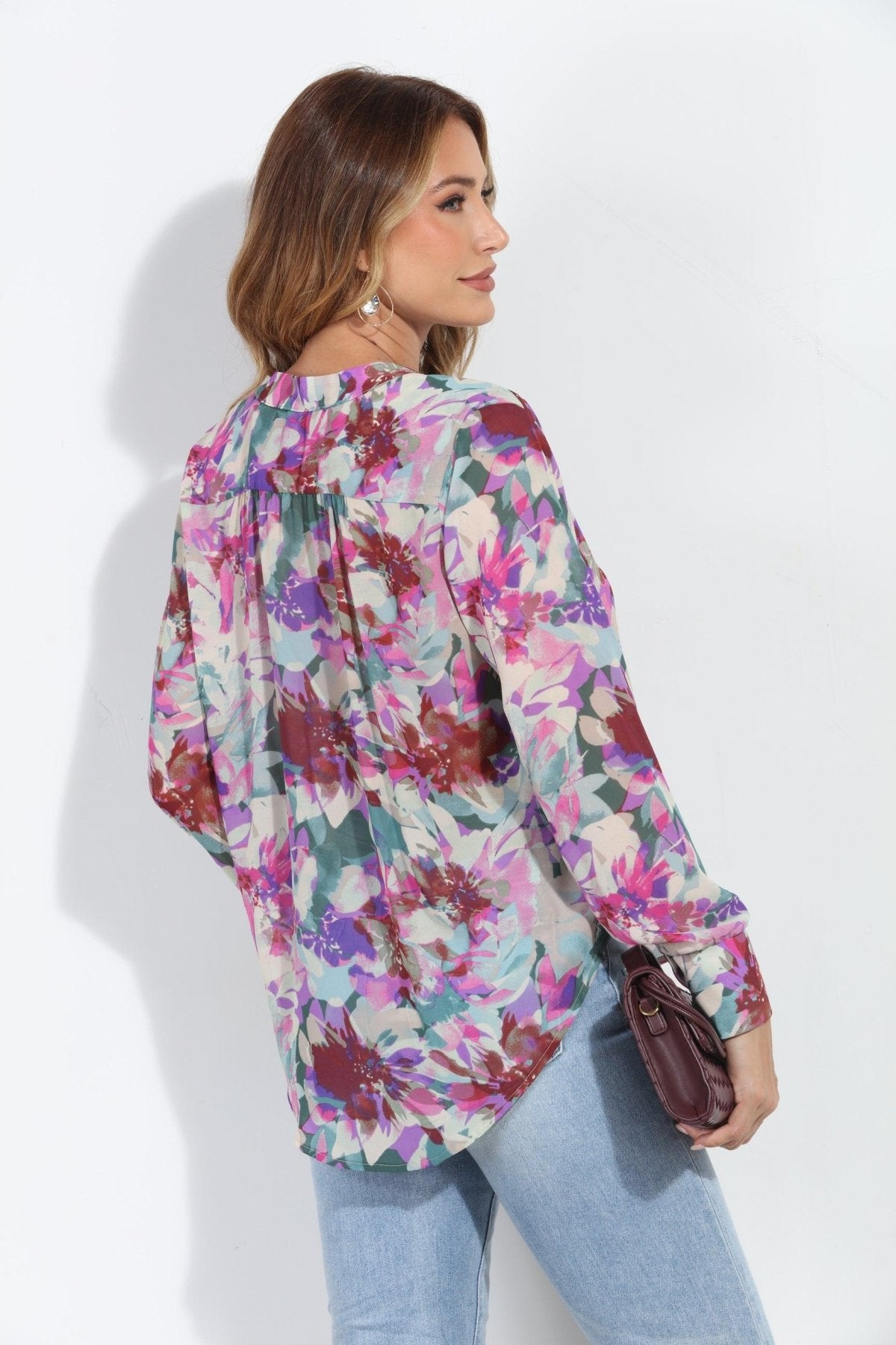 back side of floral multicolored blouse on woman in jeans and holding dark purple blouse