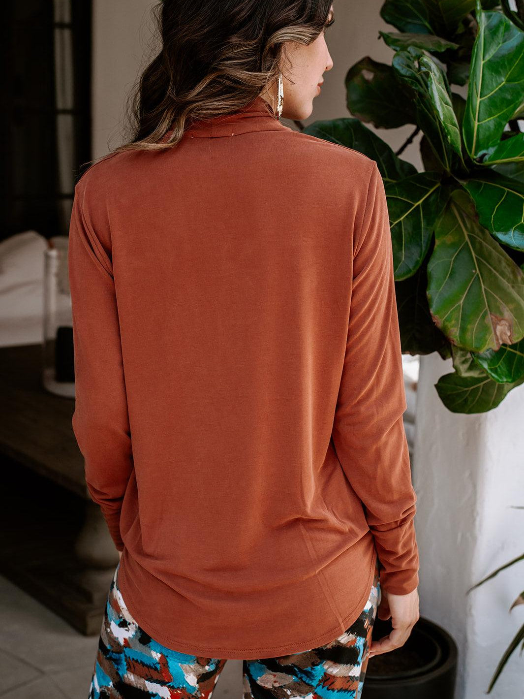 back side of dark orange long sleeve blouse on woman in multicolored pants