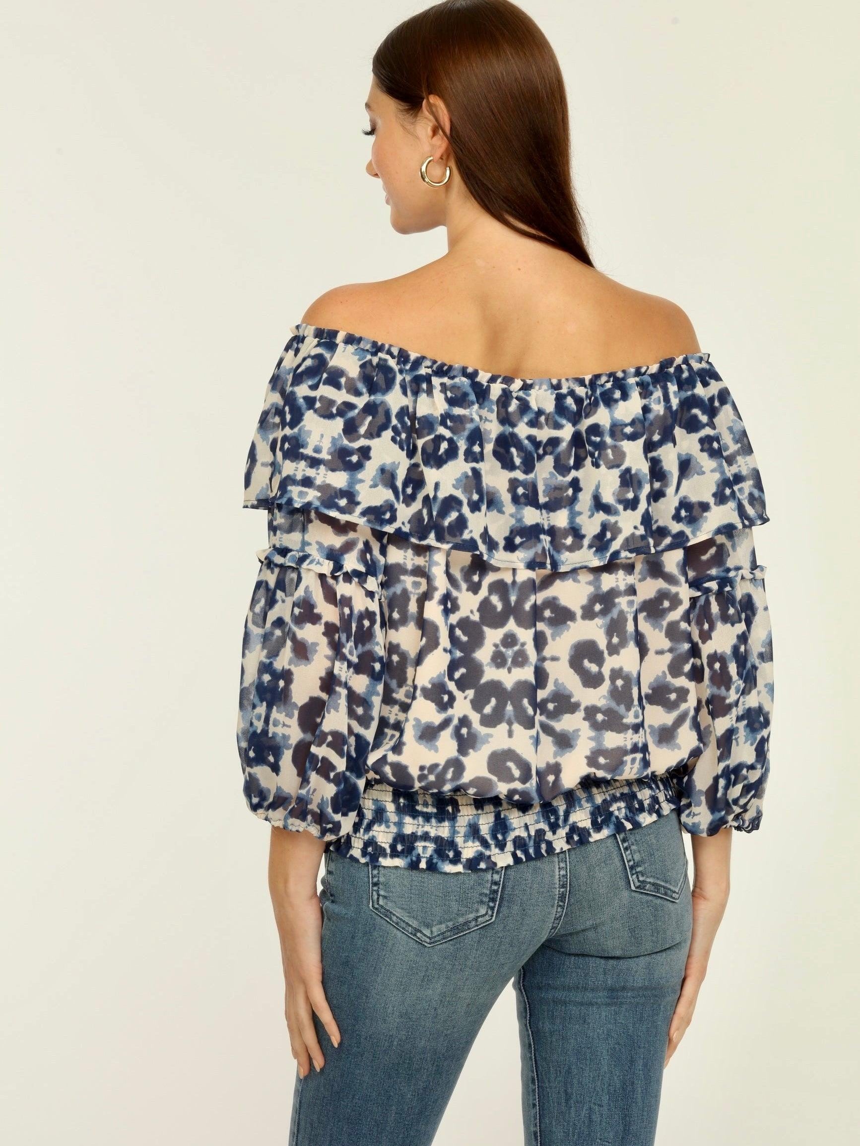 backside of blue and white printed off the shoulder blouse on woman in denim pants