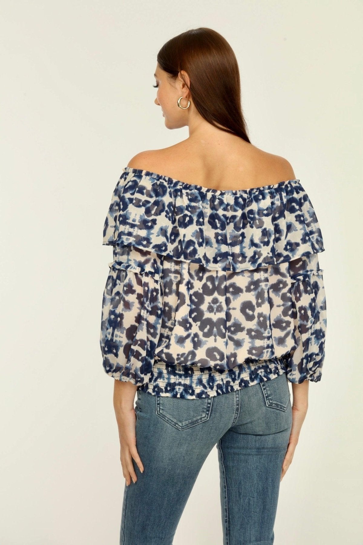 backside of blue and white printed off the shoulder blouse on woman in denim pants