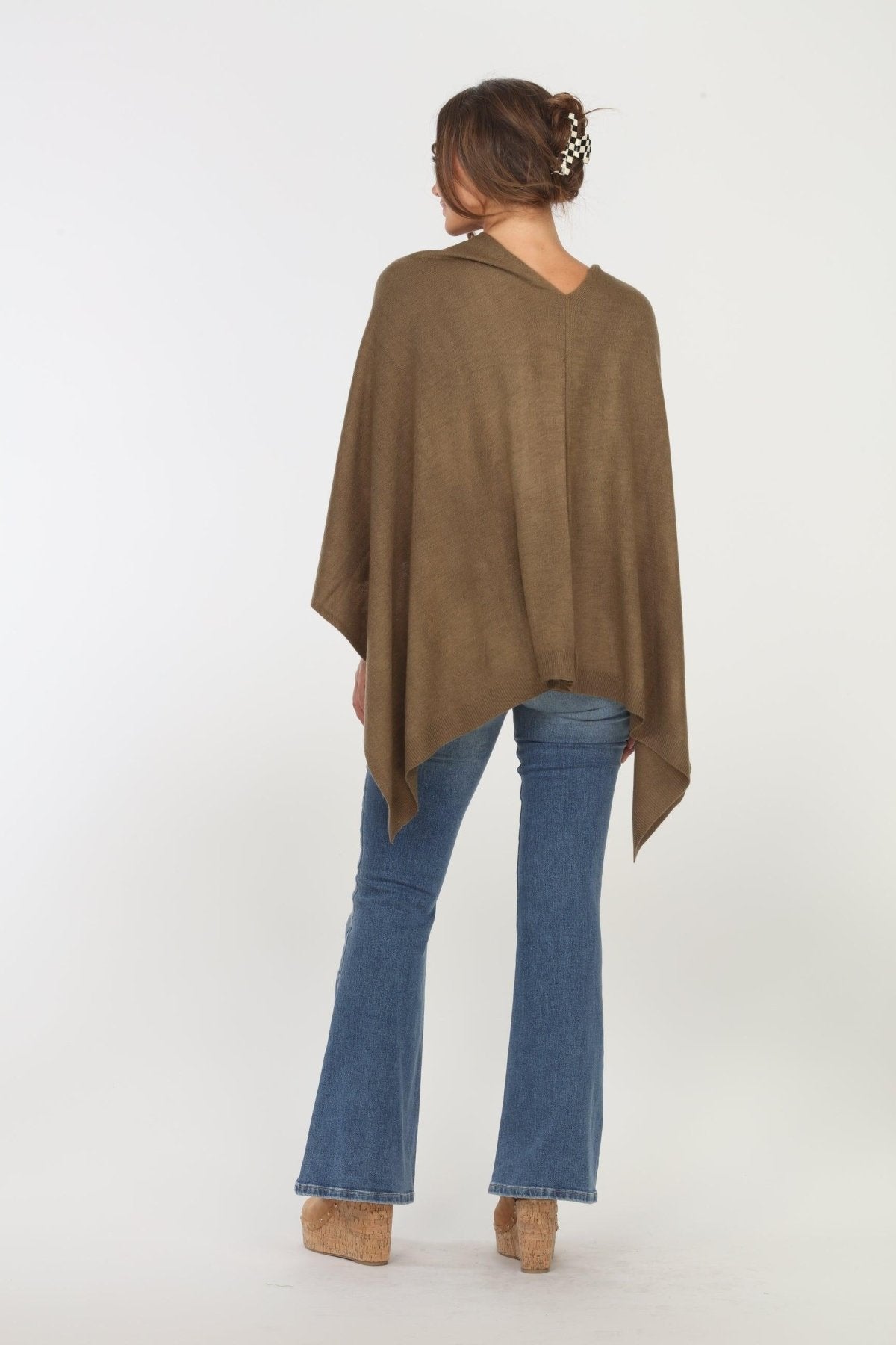 back side of olive poncho on woman in denim pants and tan shoes