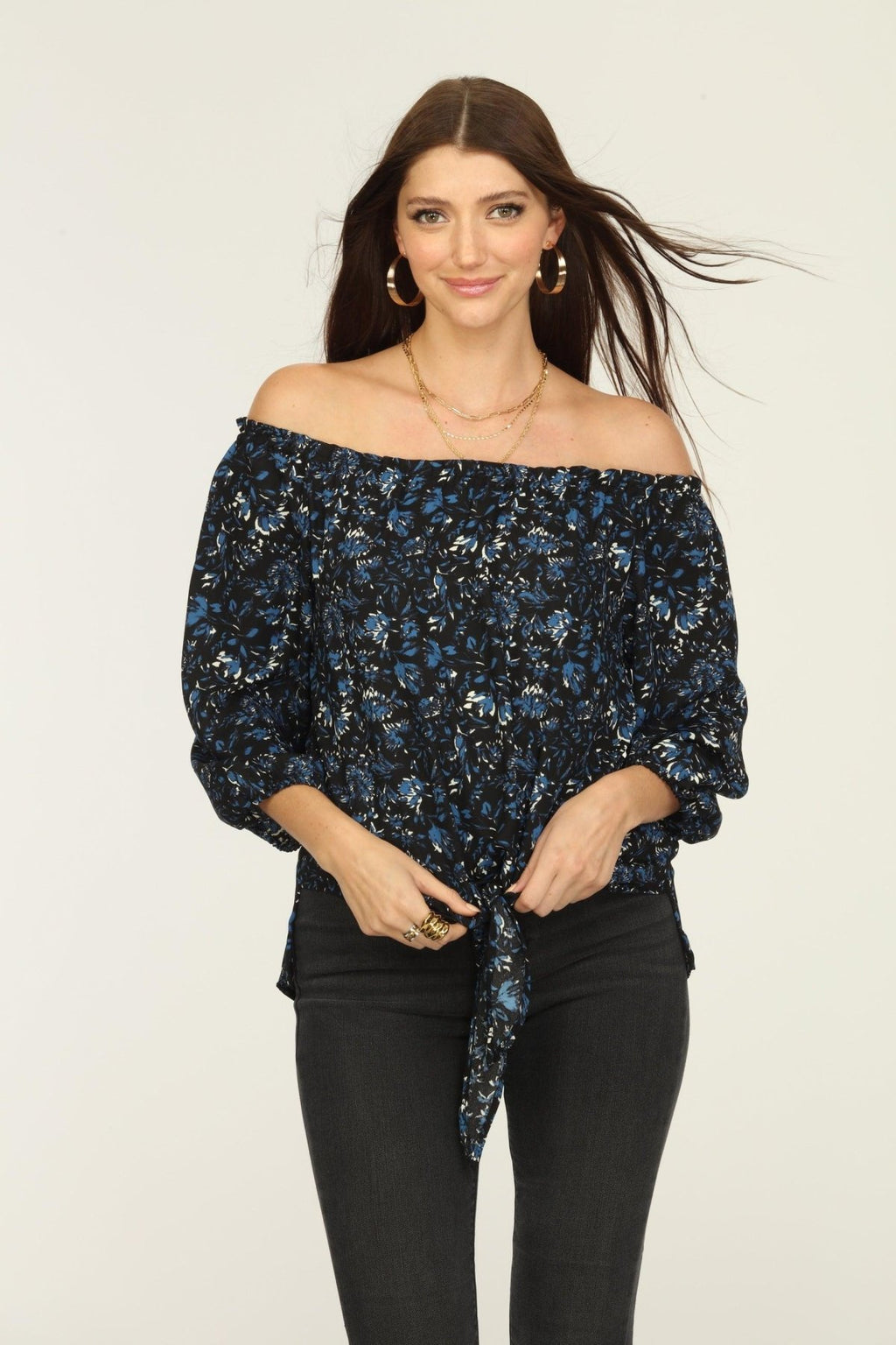 black and blue off the shoulder blouse on woman in dark denim pants