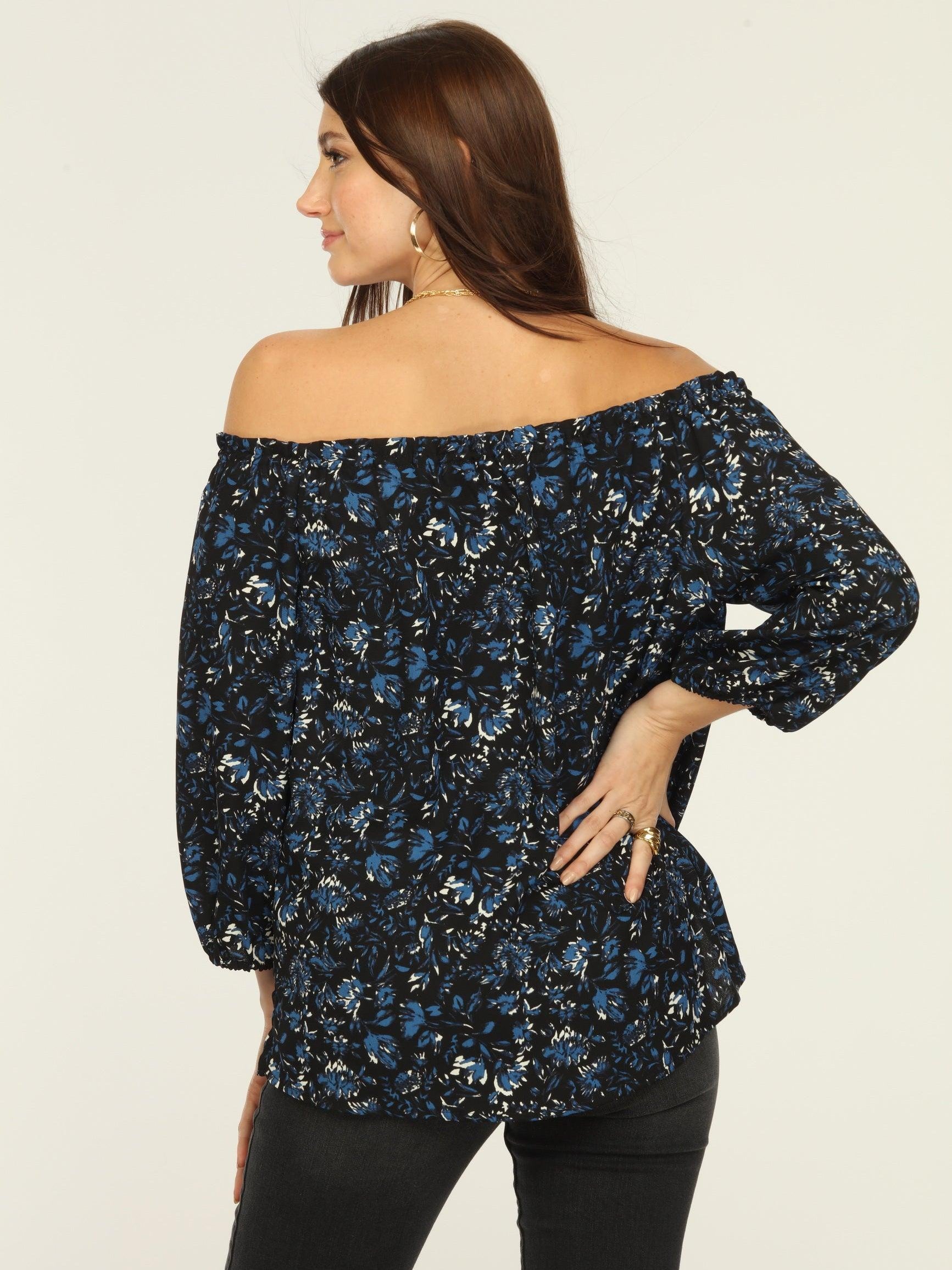 back side of black and blue off the shoulder blouse on woman in dark denim pants
