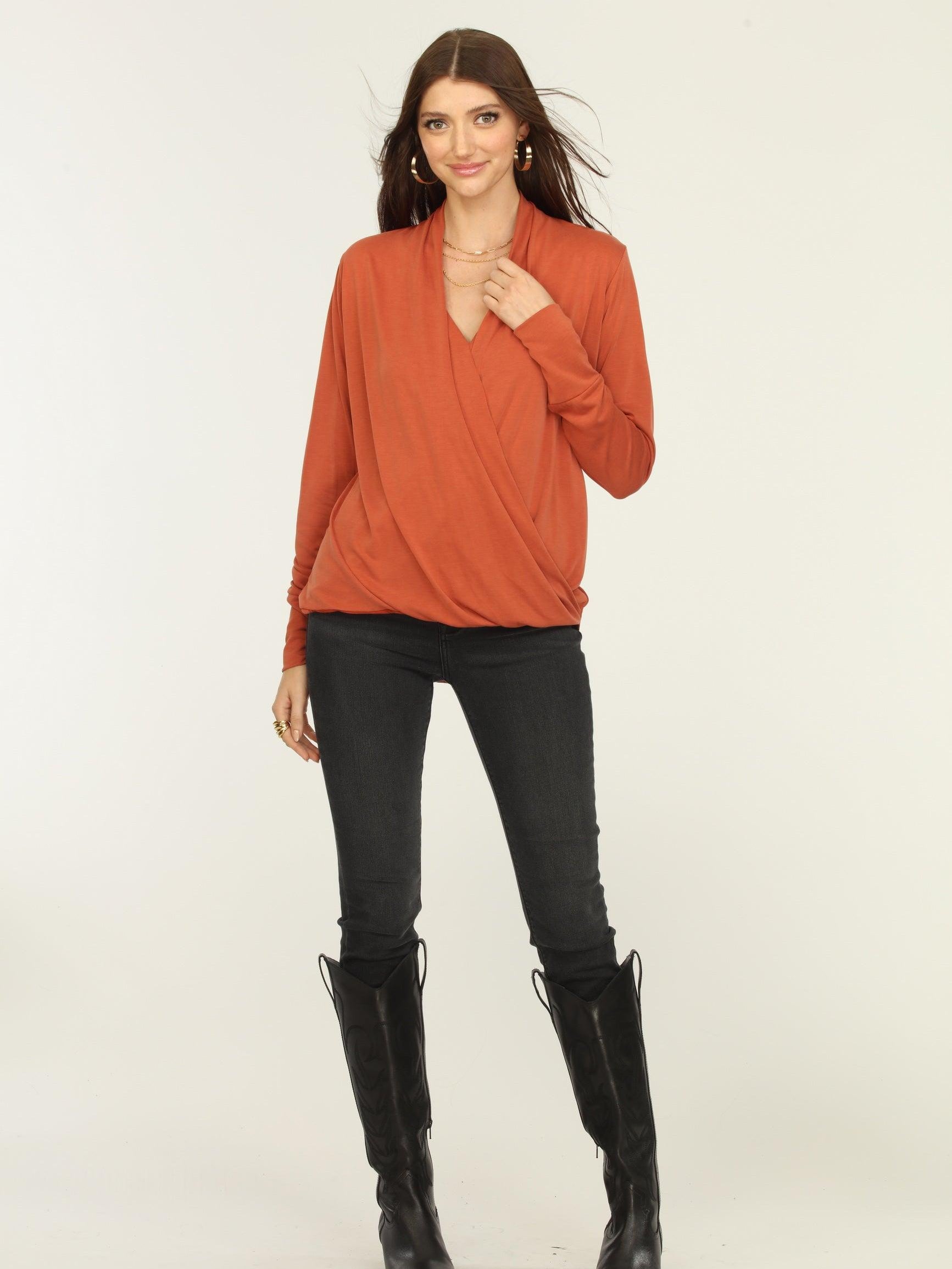 orange long sleeve draped top on woman in dark jeans and black boots