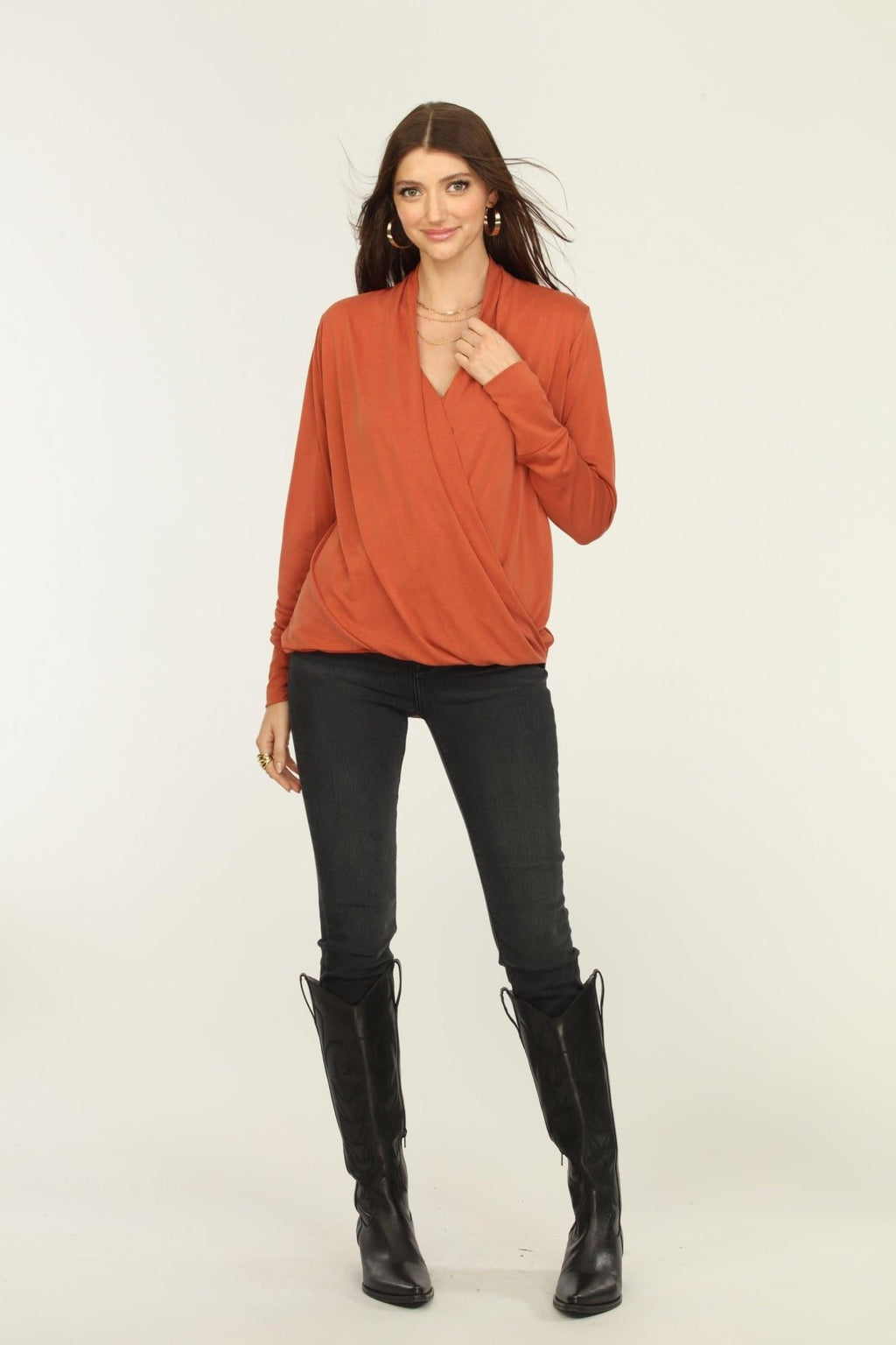 orange long sleeve draped top on woman in dark jeans and black boots
