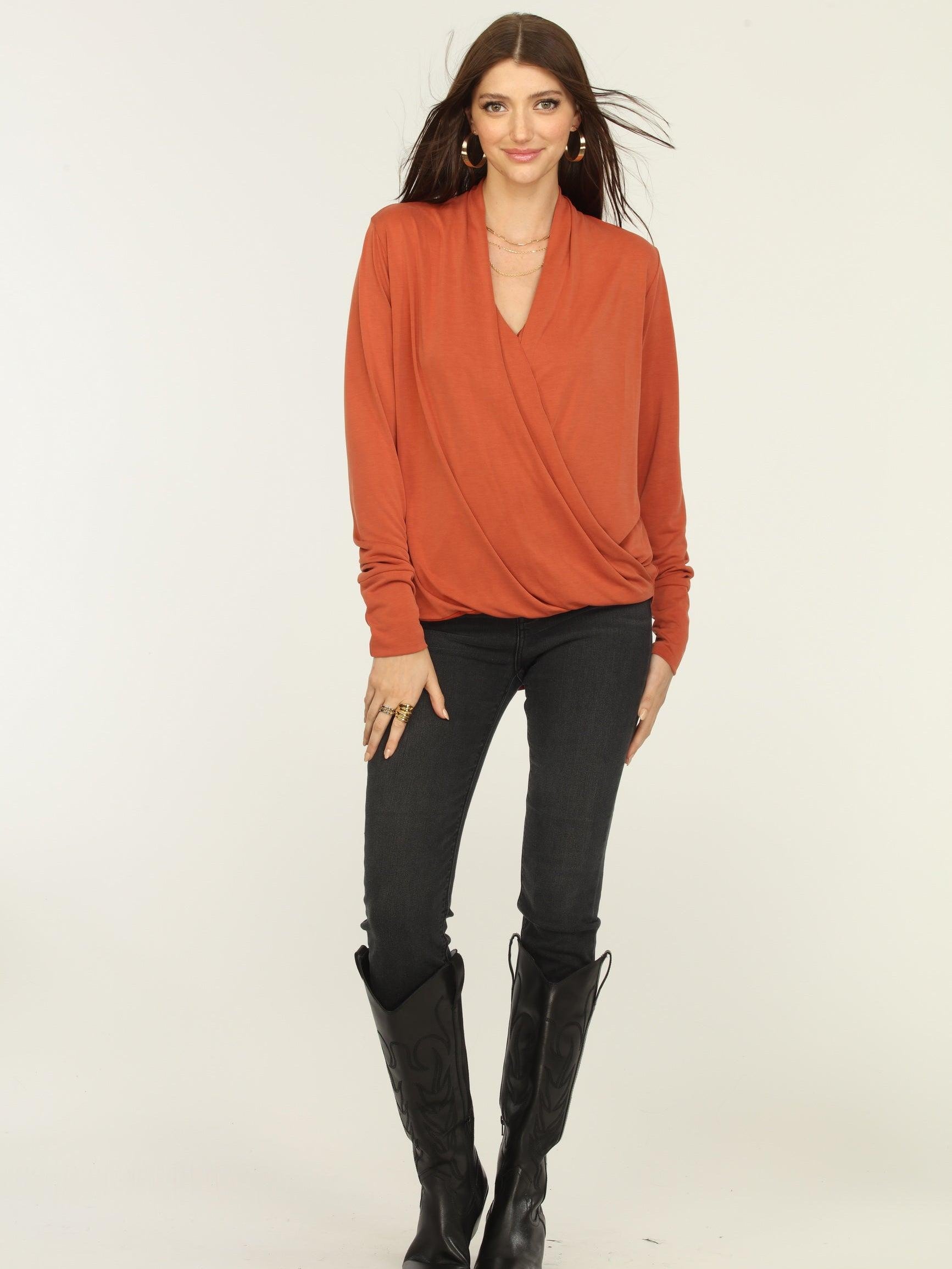 orange long sleeve draped top on woman in dark jeans and black boots
