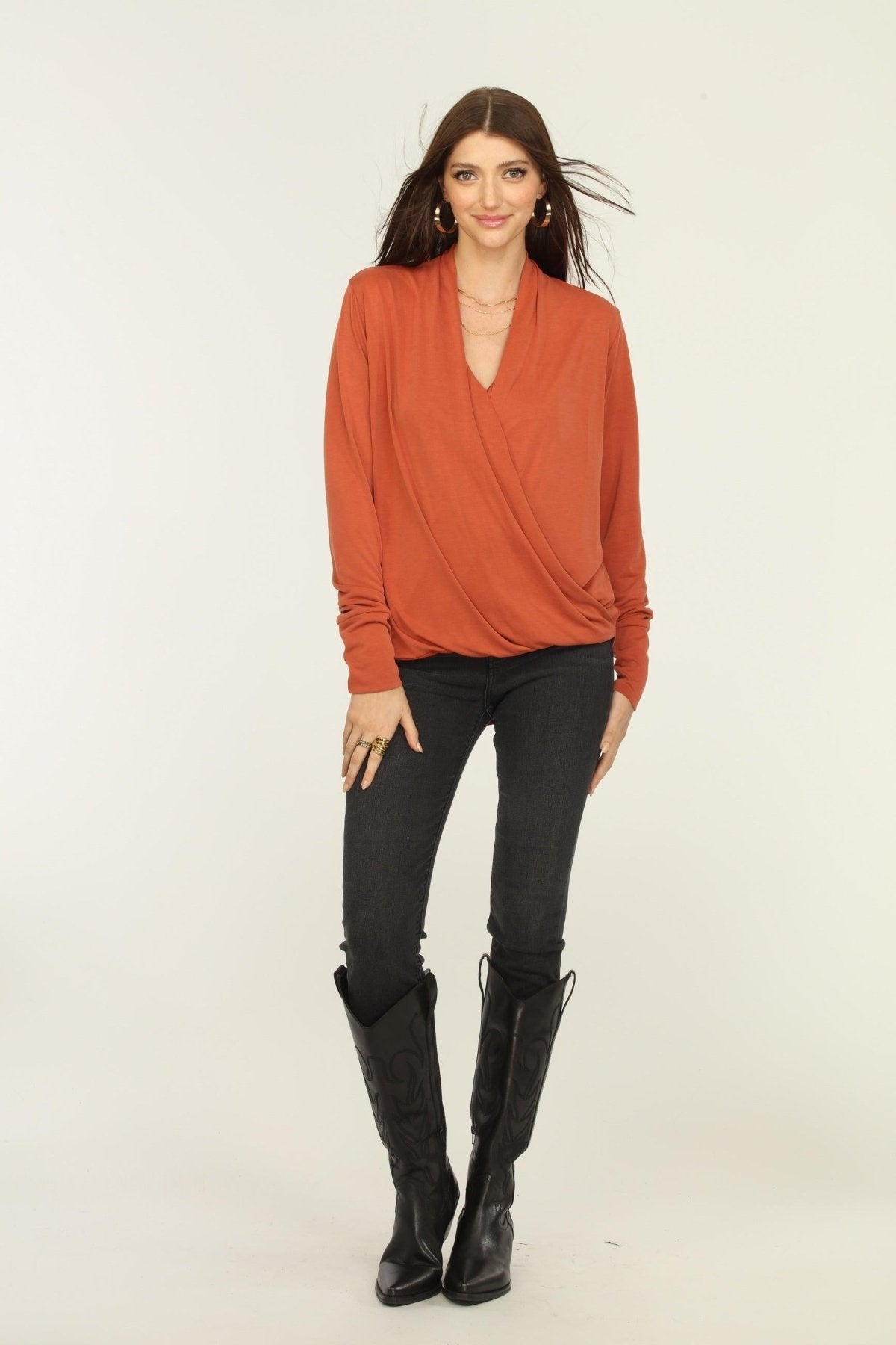 orange long sleeve draped top on woman in dark jeans and black boots