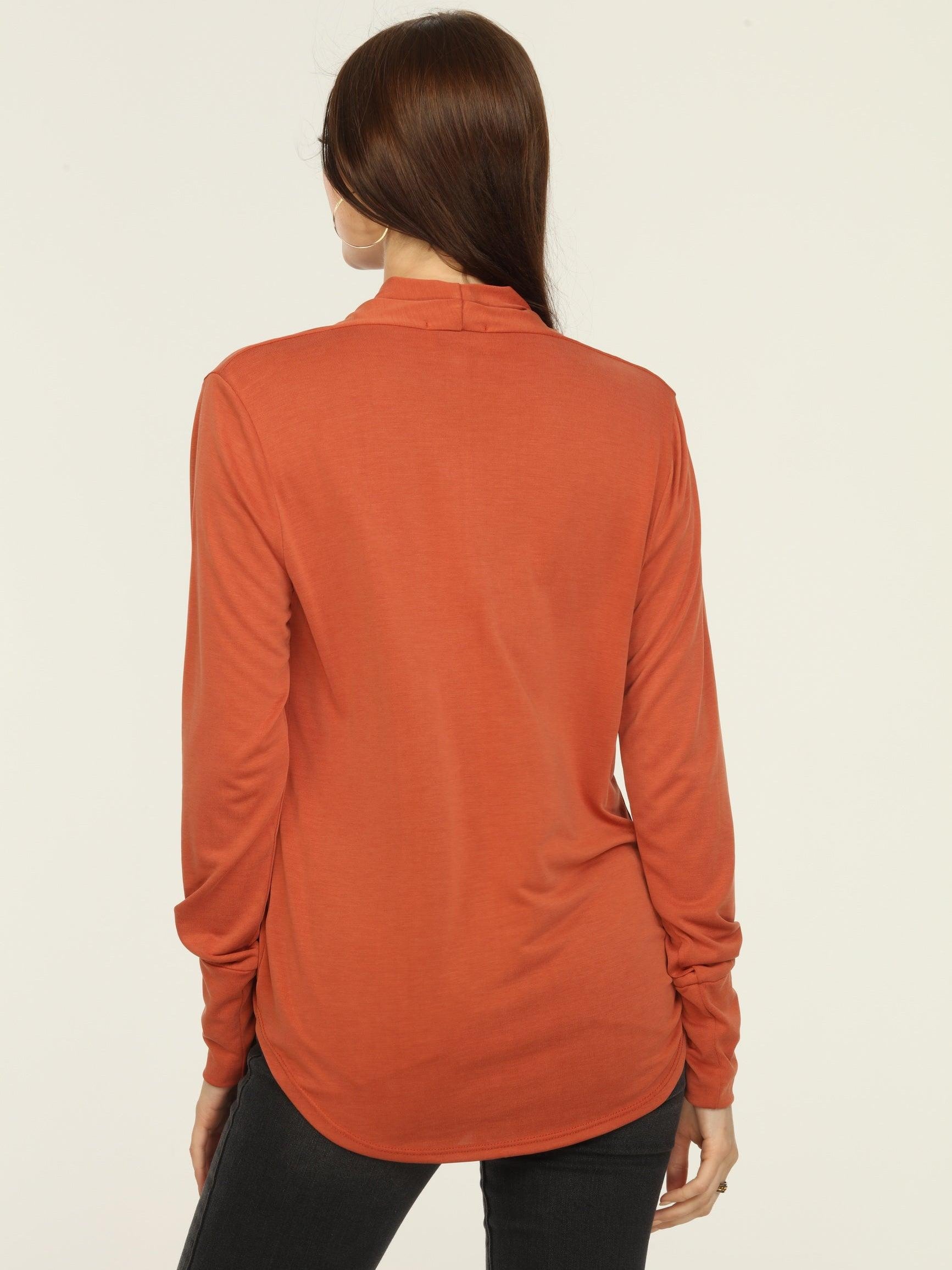 back side of orange long sleeve draped top on woman in dark jeans