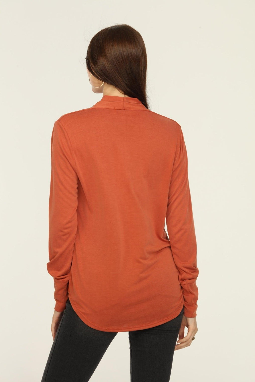 back side of orange long sleeve draped top on woman in dark jeans