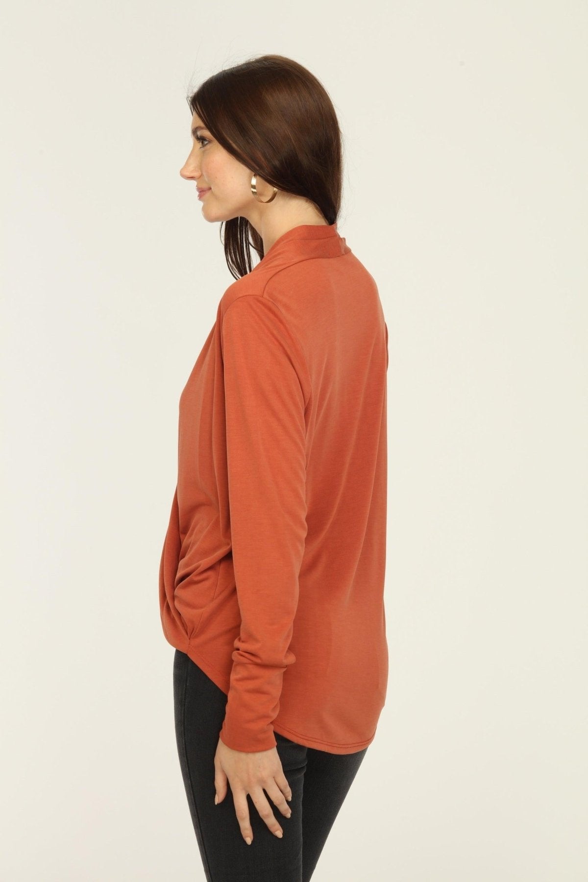 side view of orange long sleeve draped top on woman in dark jeans