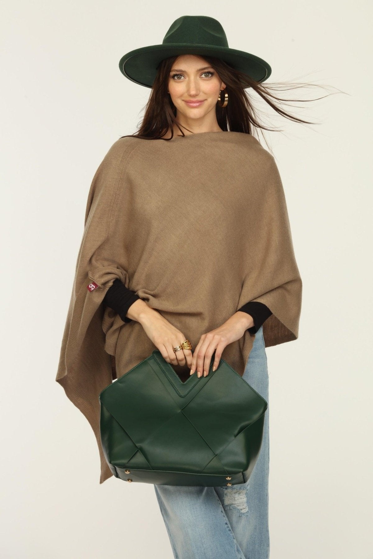 woman wearing a hat, tan poncho and jeans, holding green purse