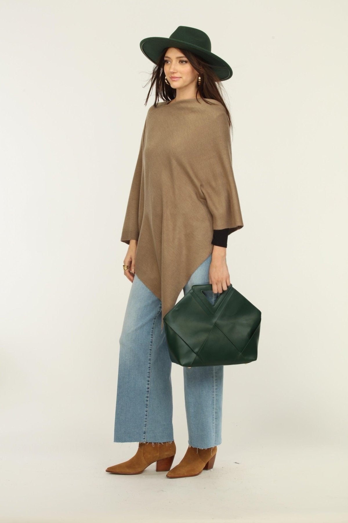 woman wearing a hat, tan poncho, jeans, and tan boots holding green purse