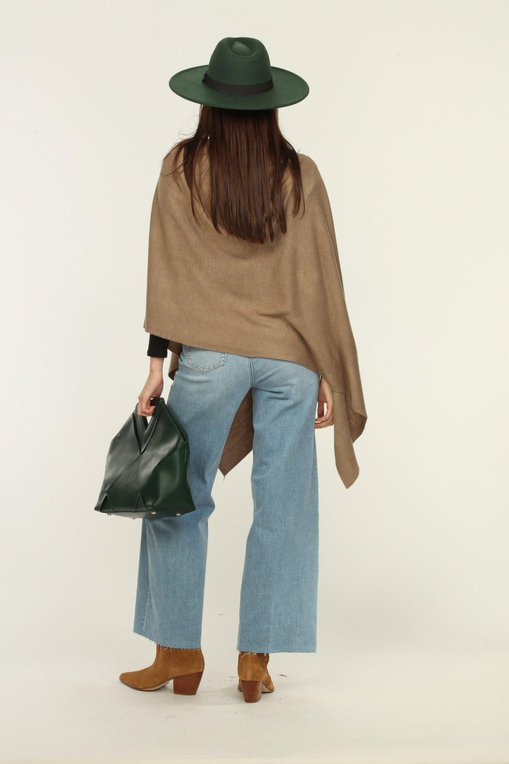 back side of woman wearing a hat, tan poncho, jeans, and tan boots