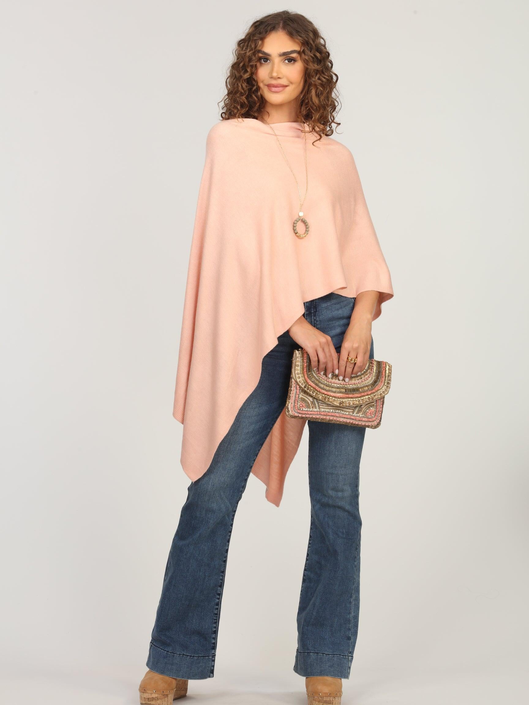 light pink poncho on woman in dark denim pants and holding multicolored purse