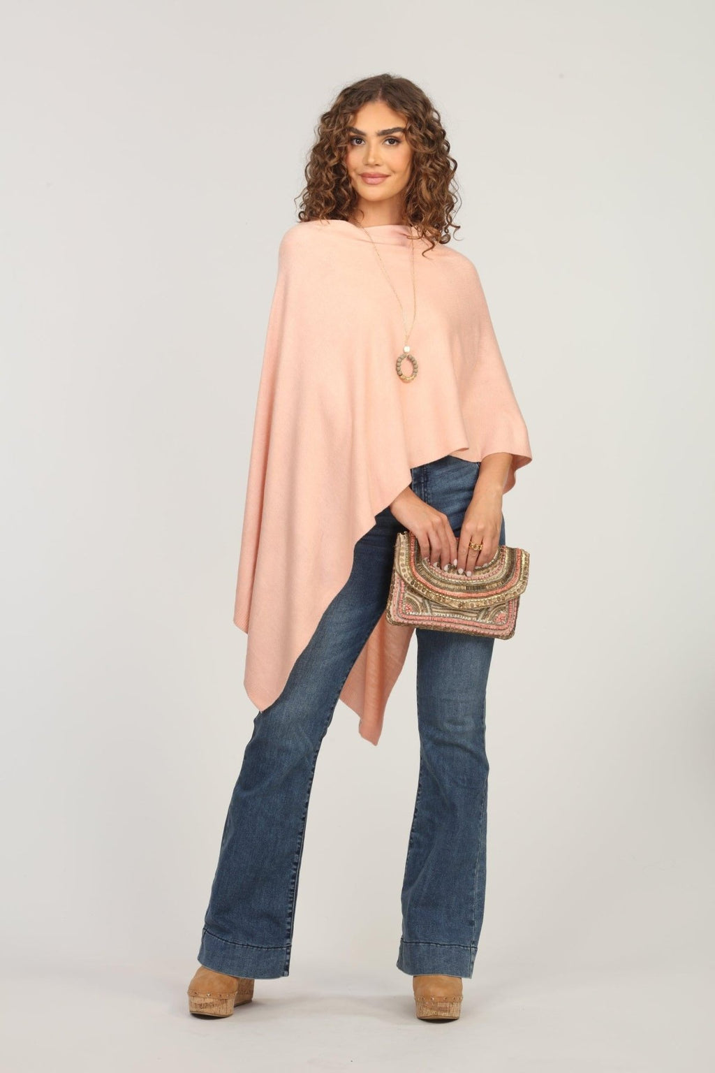 light pink poncho on woman in dark denim pants and holding multicolored purse