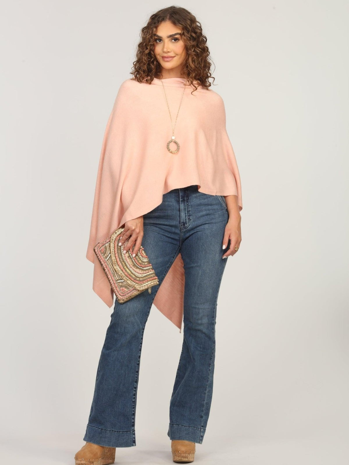 light pink poncho on woman in dark denim pants and holding multicolored purse