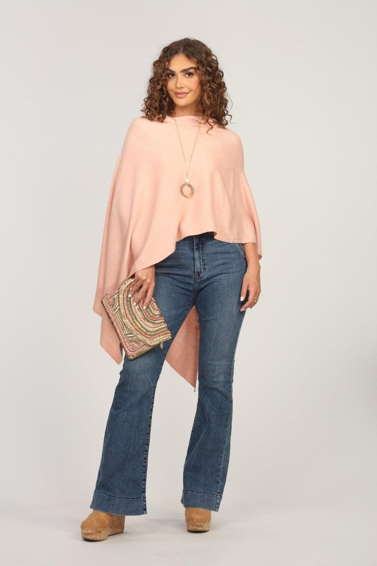 light pink poncho on woman in dark denim pants and holding multicolored purse
