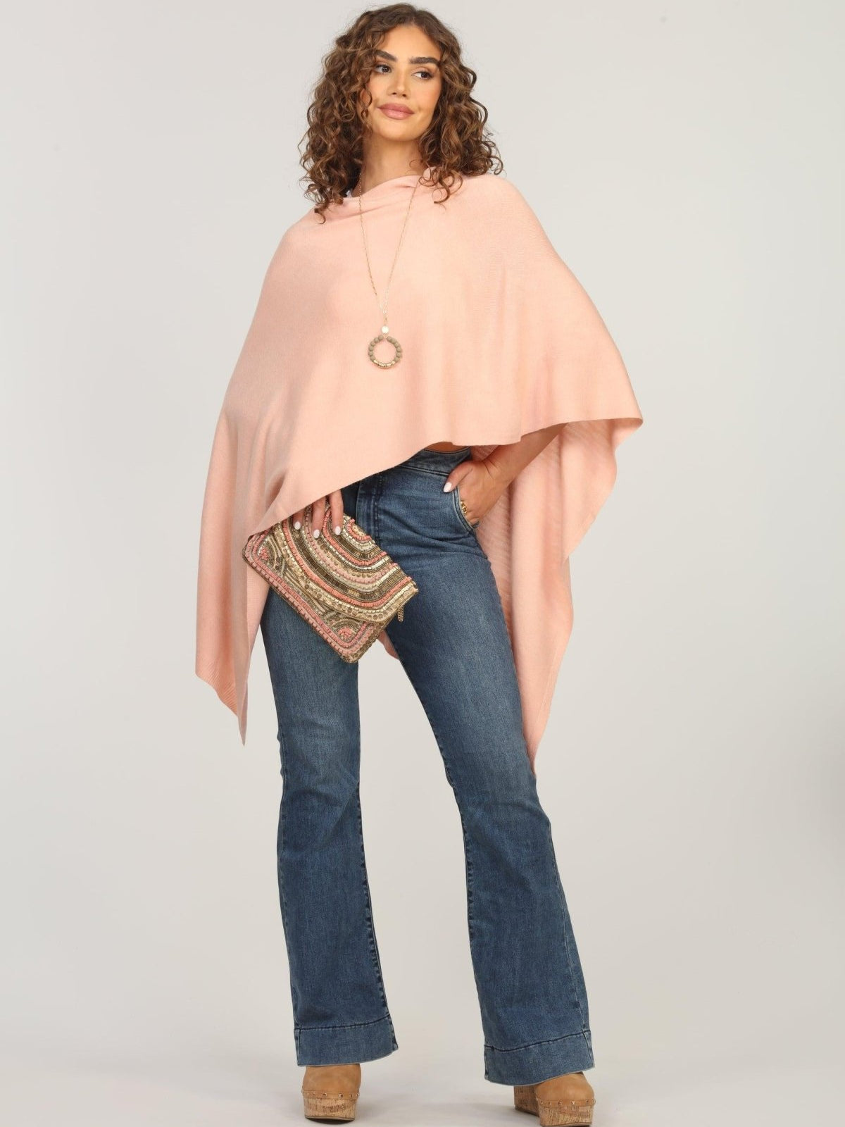 light pink poncho on woman in dark denim pants and holding multicolored purse