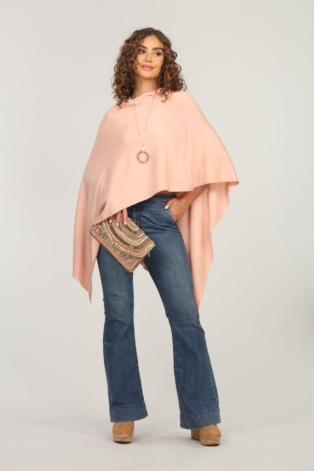 light pink poncho on woman in dark denim pants and holding multicolored purse