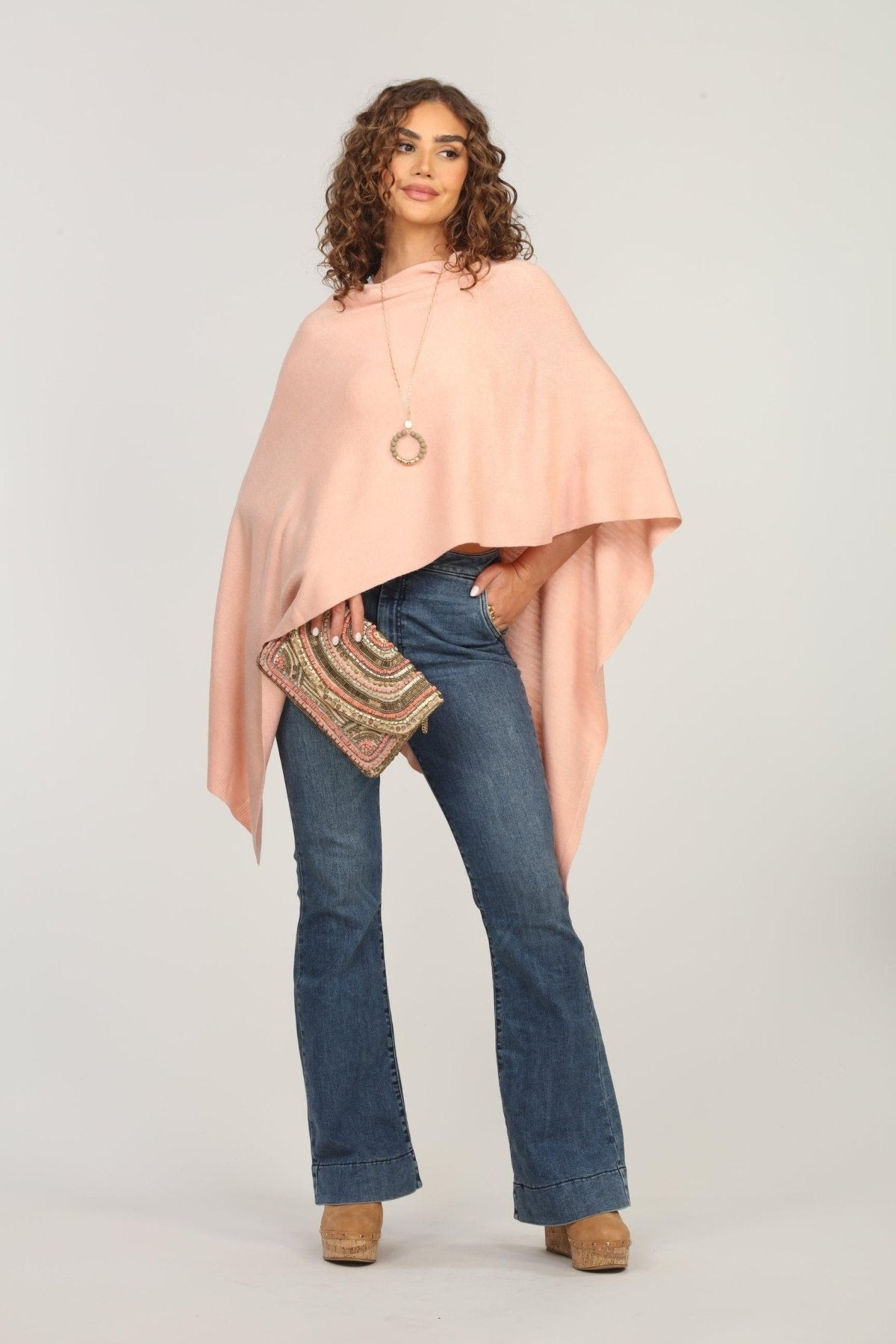 light pink poncho on woman in dark denim pants and holding multicolored purse