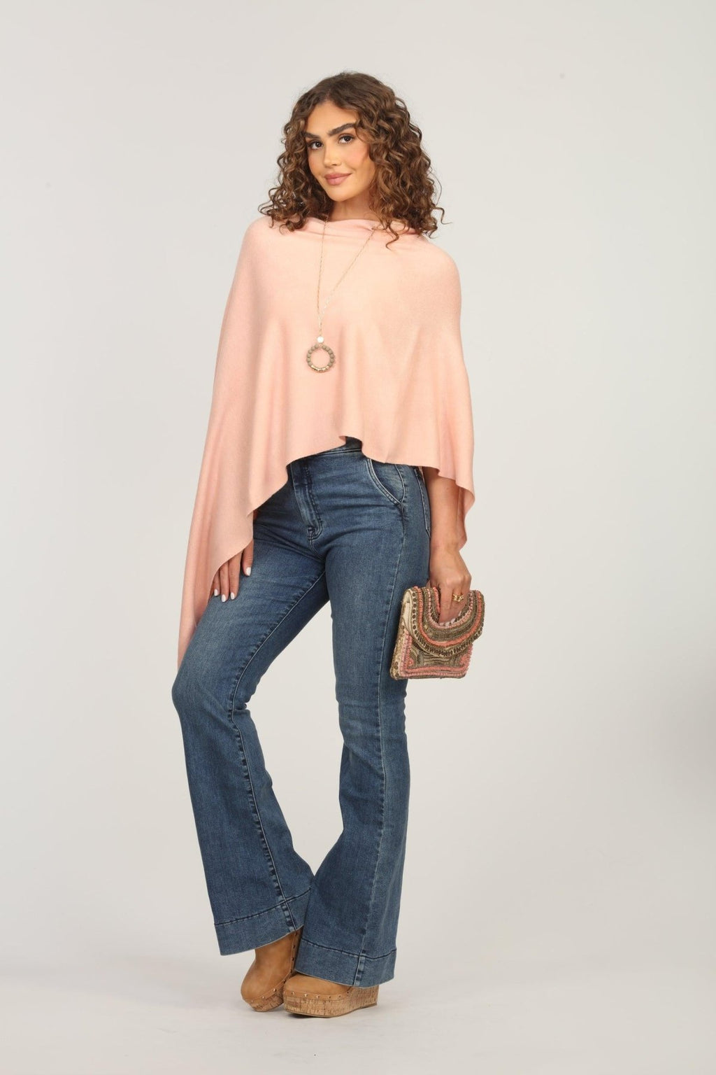 light pink poncho on woman in dark denim pants and holding multicolored purse