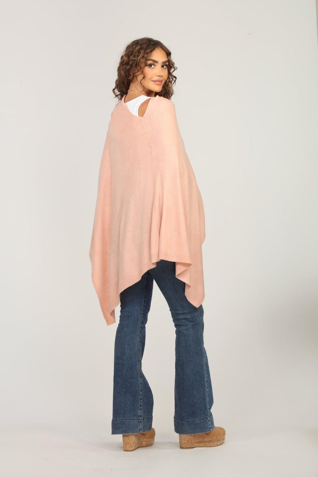 back side of light pink poncho on woman in dark denim pants