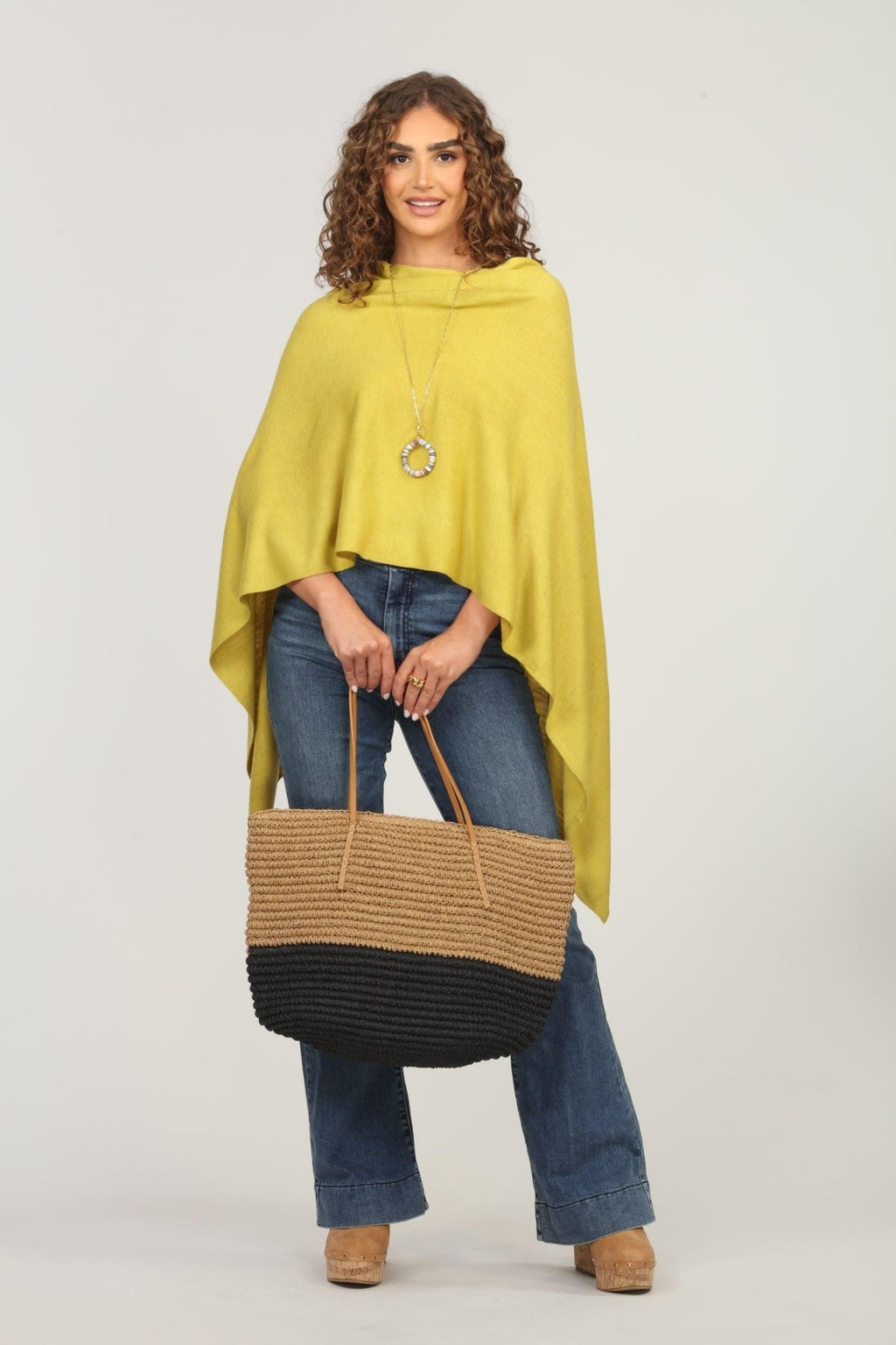 lime green poncho and dark denim jeans on woman holding woven tote bag