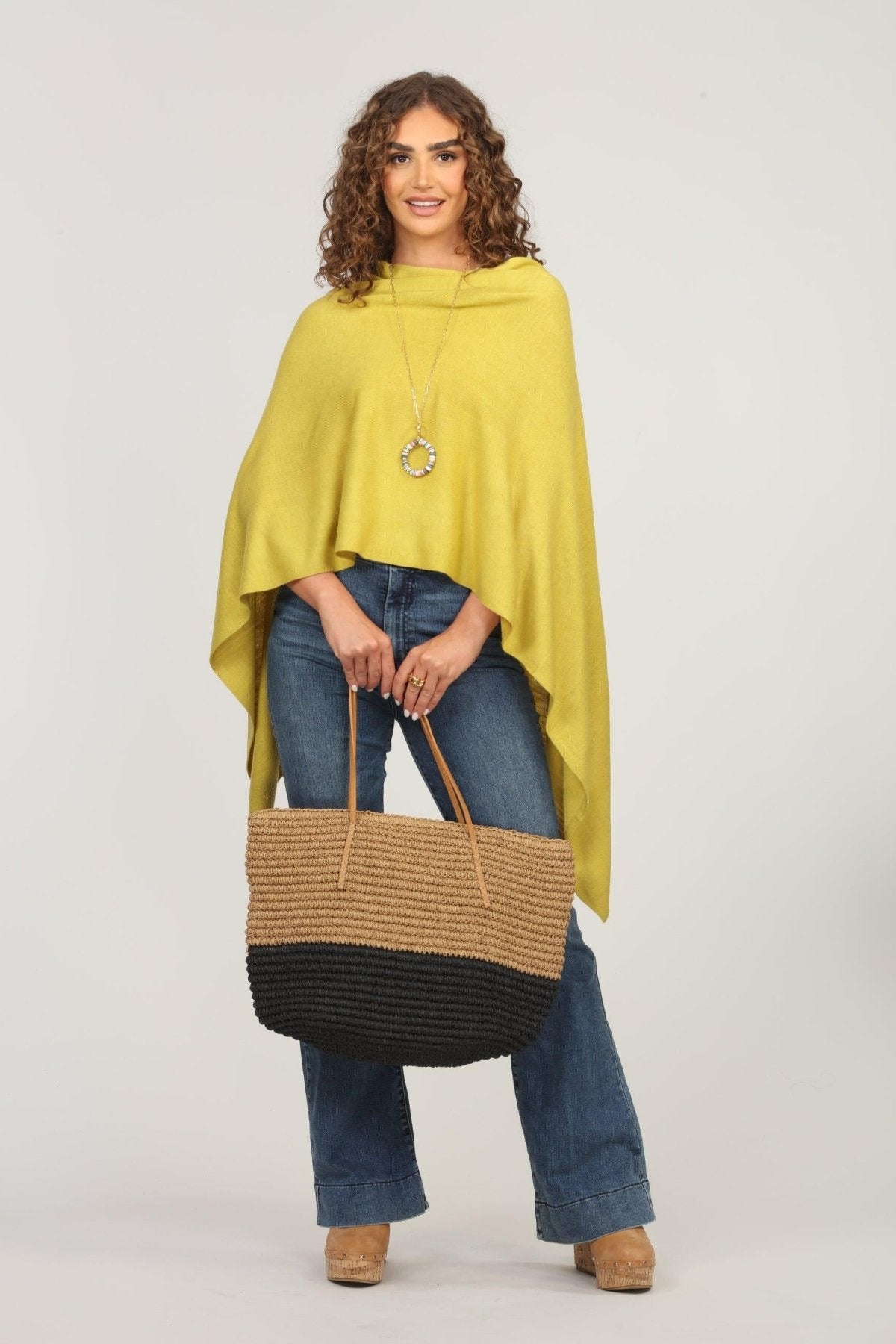 lime green poncho and dark denim jeans on woman holding woven tote bag
