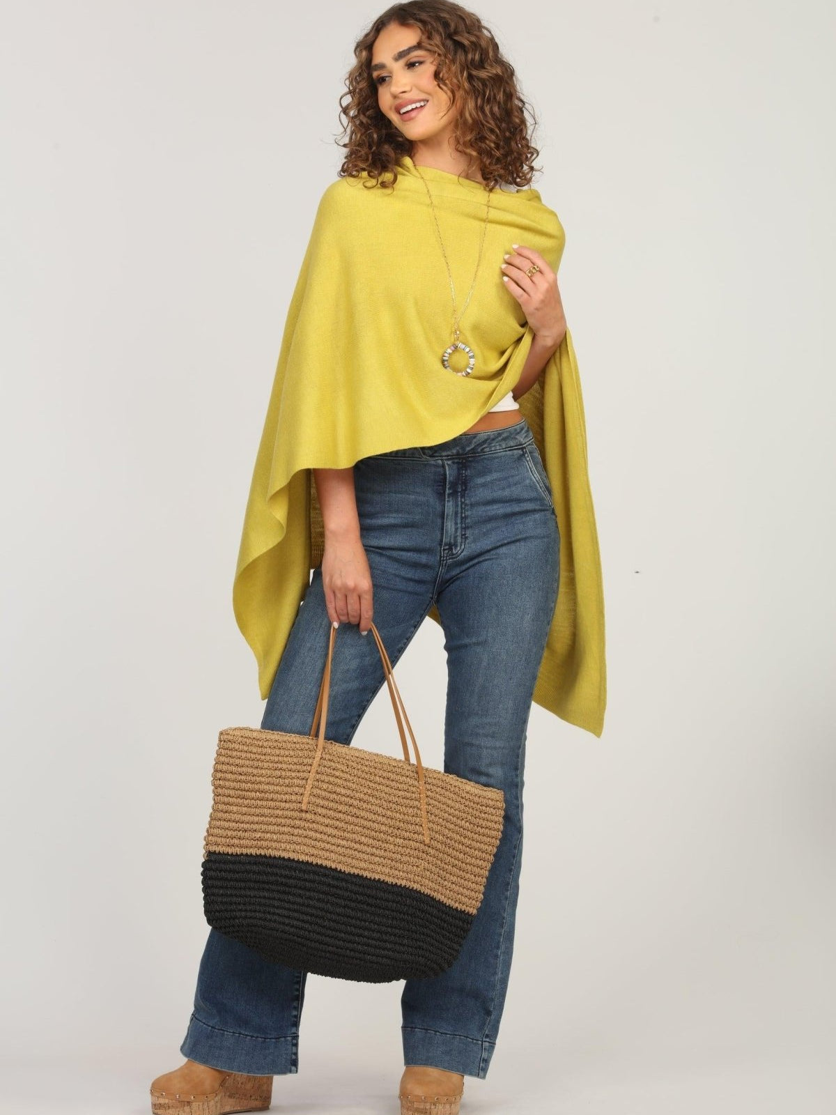 lime green poncho and dark denim jeans on woman holding woven tote bag
