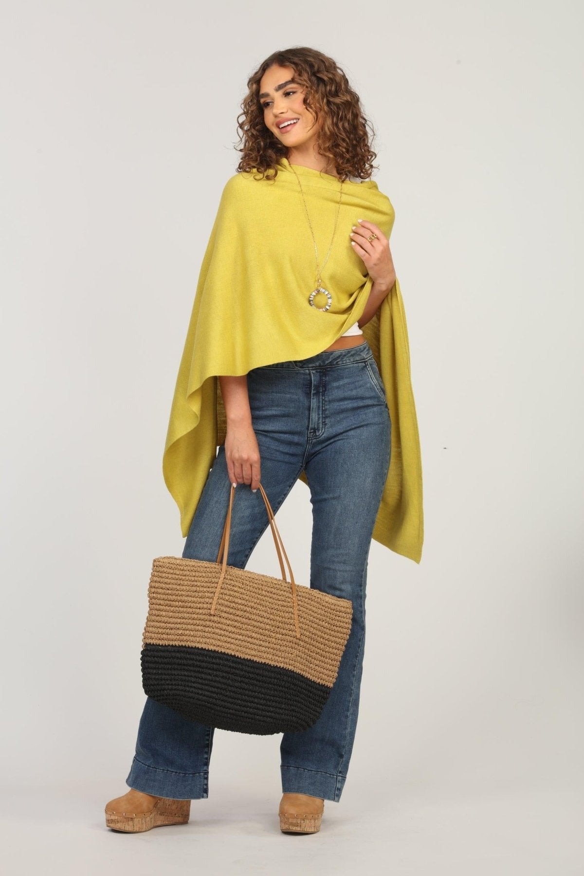 lime green poncho and dark denim jeans on woman holding woven tote bag