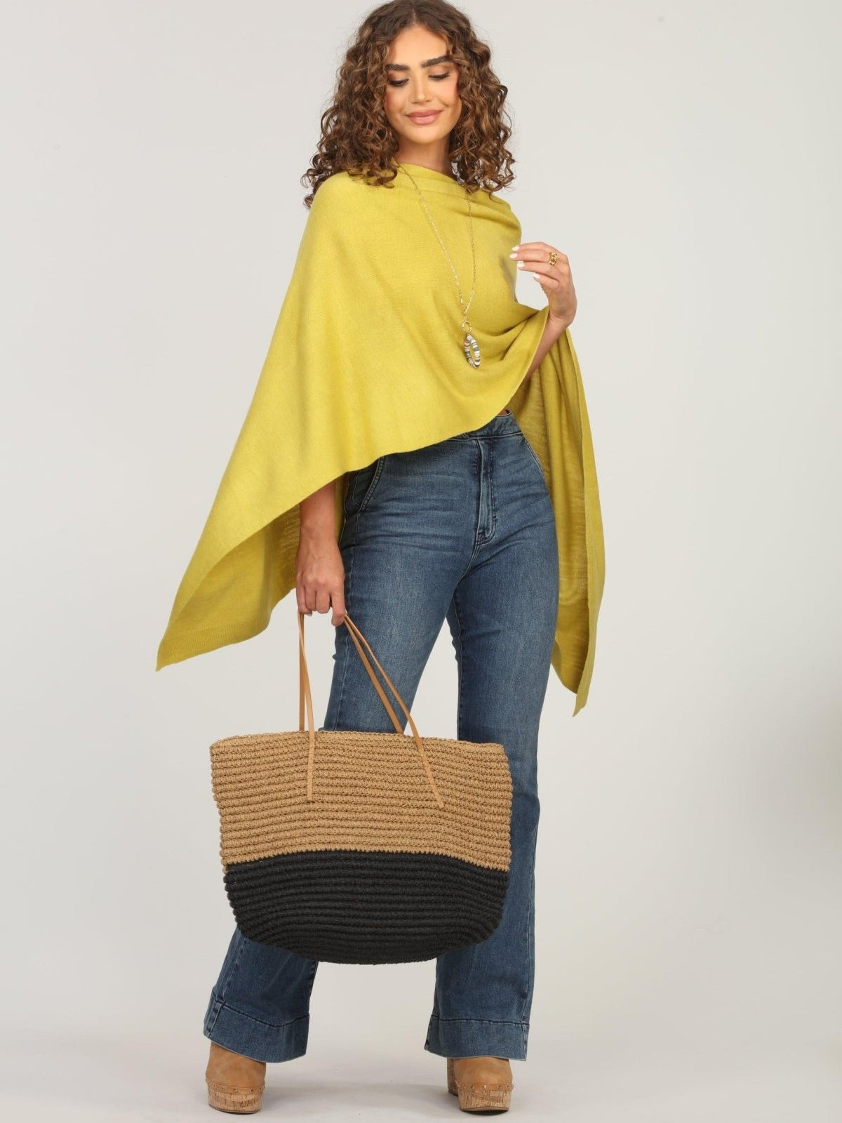 lime green poncho and dark denim jeans on woman holding woven tote bag