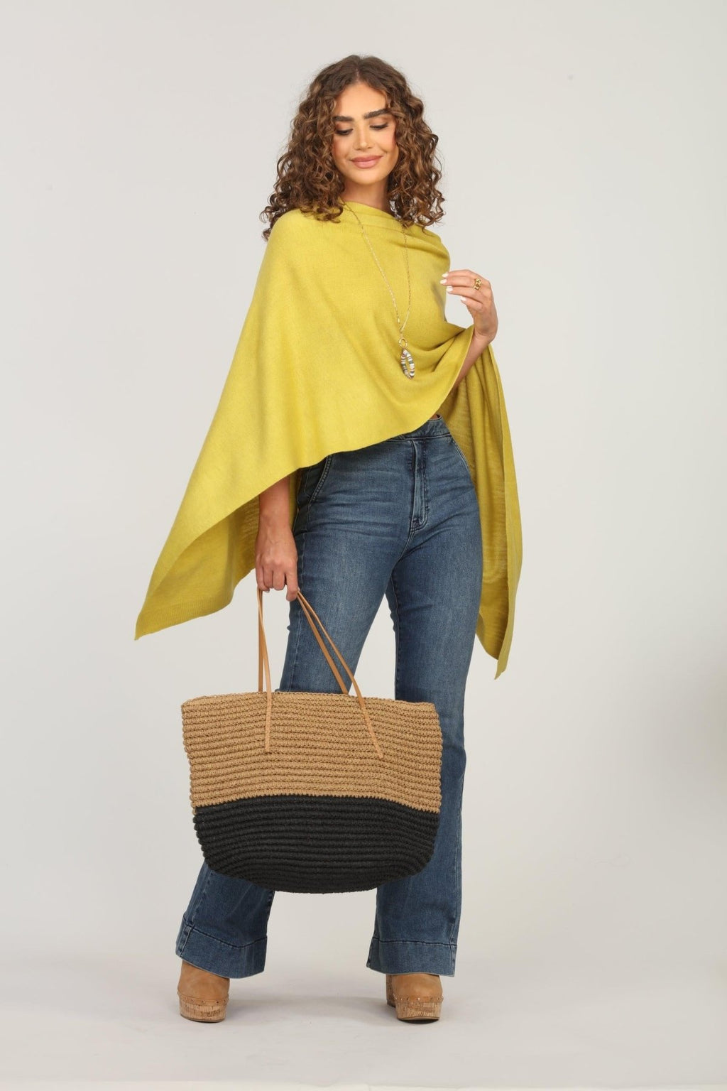 lime green poncho and dark denim jeans on woman holding woven tote bag