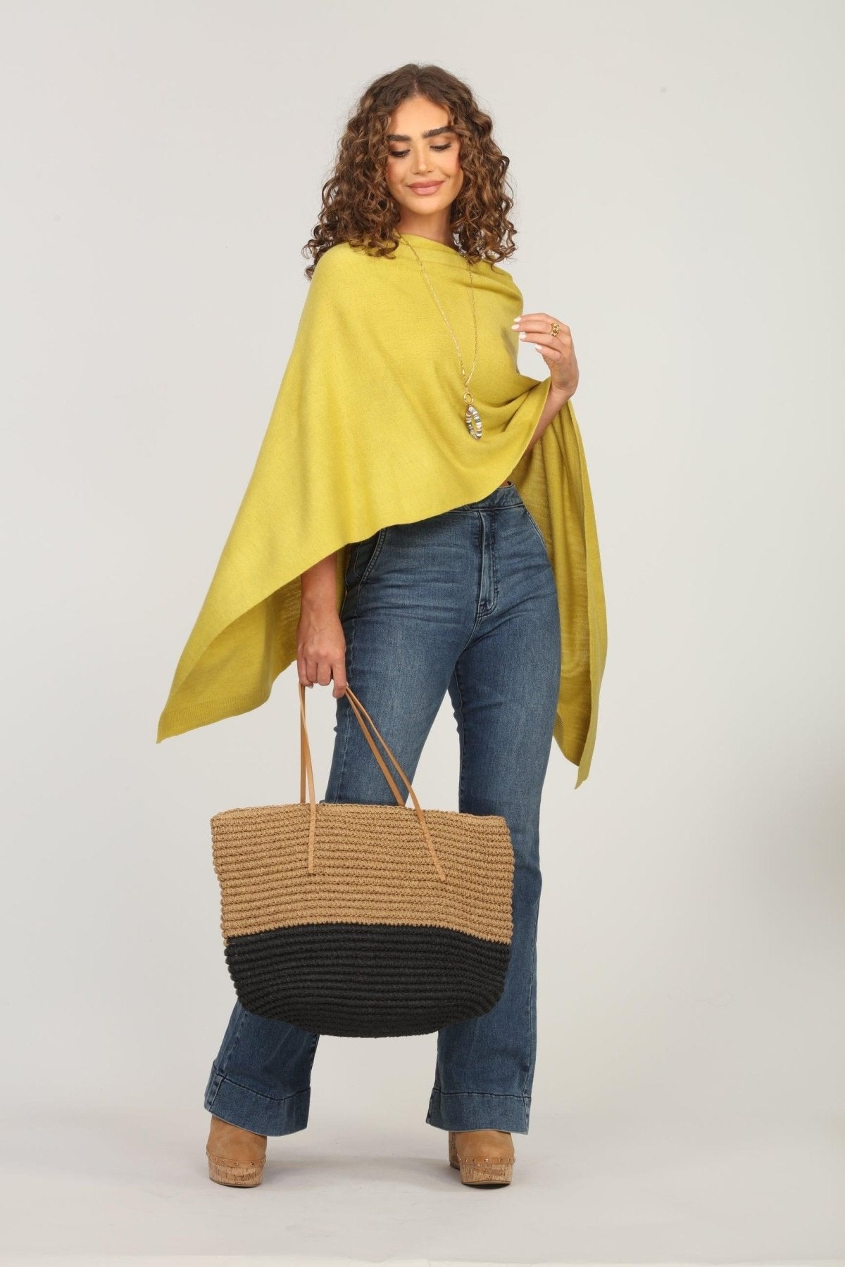 lime green poncho and dark denim jeans on woman holding woven tote bag
