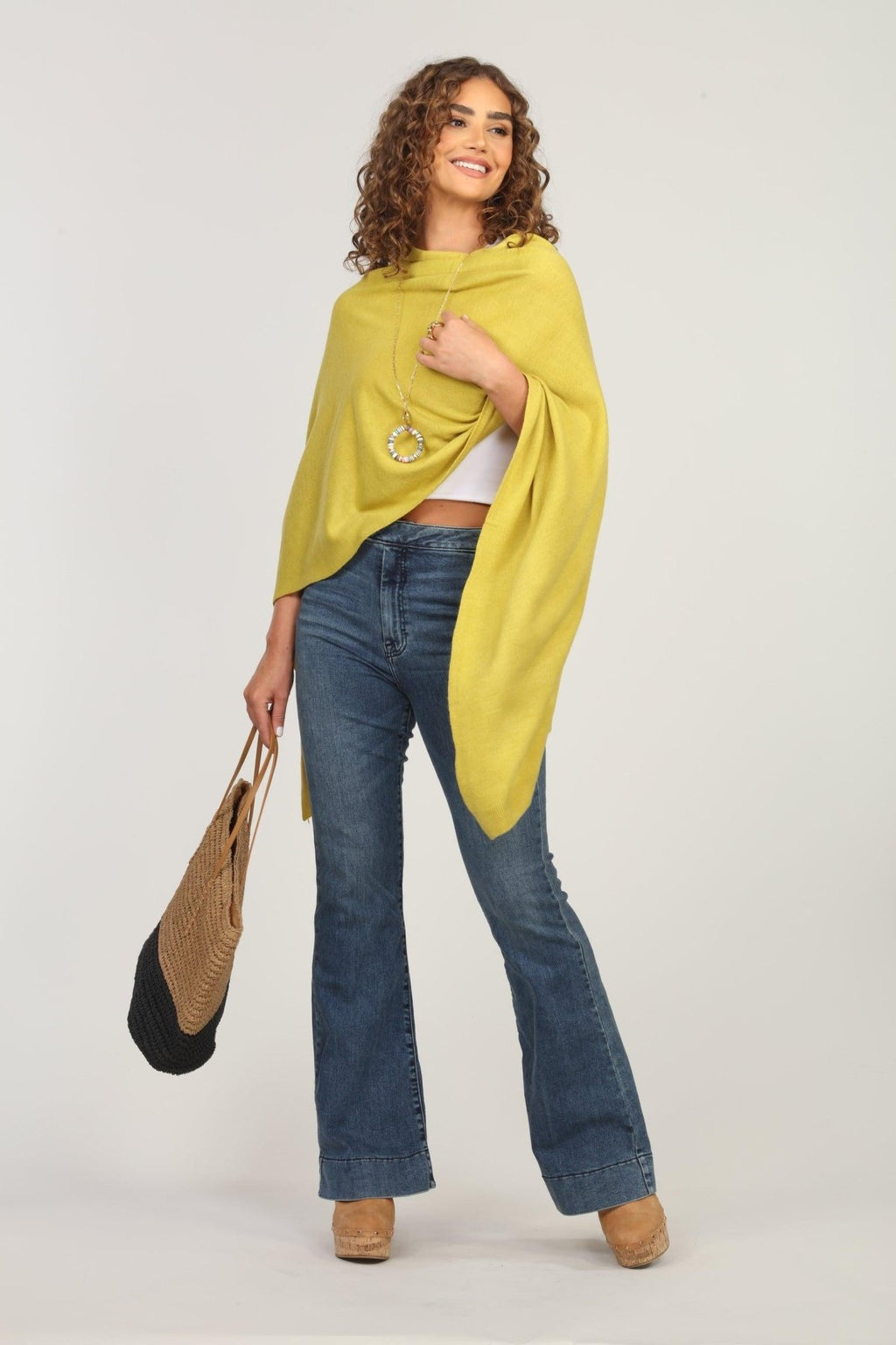 lime green poncho and dark denim jeans on woman holding woven tote bag