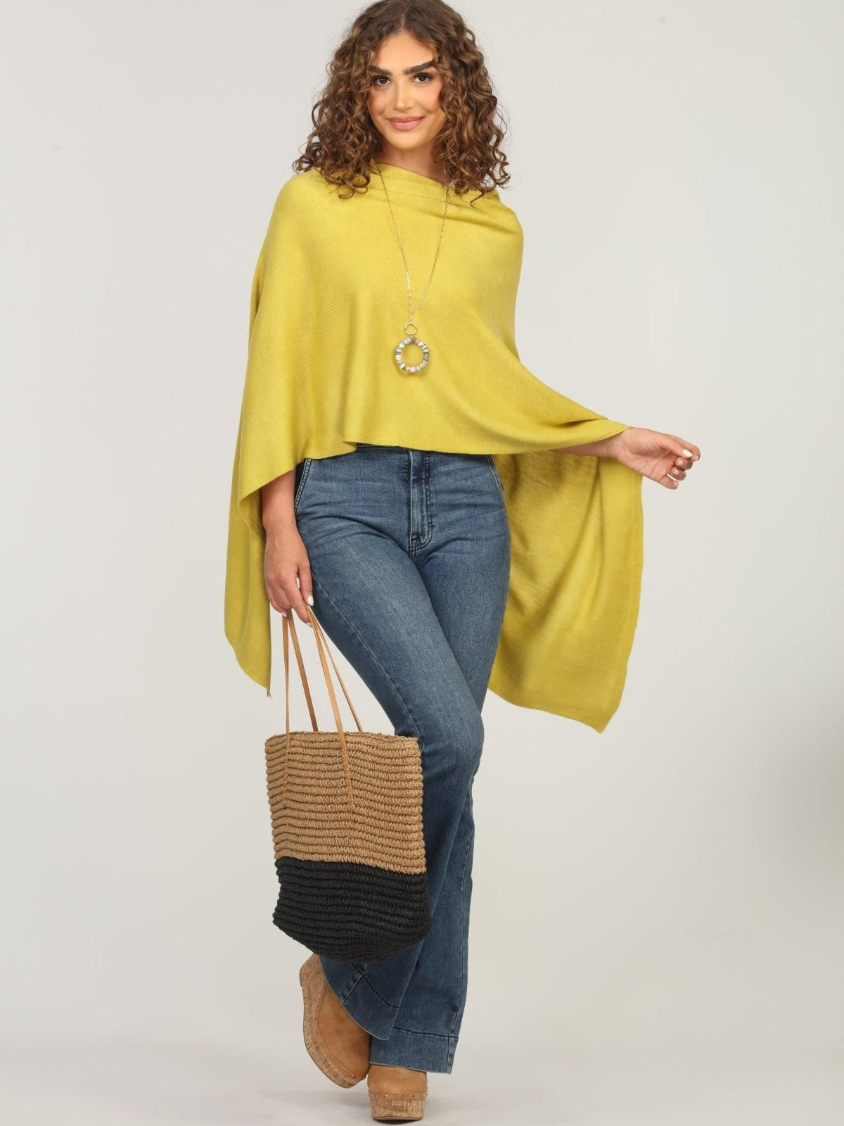 lime green poncho and dark denim jeans on woman holding woven tote bag