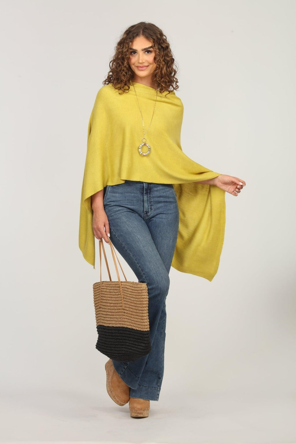 lime green poncho and dark denim jeans on woman holding woven tote bag