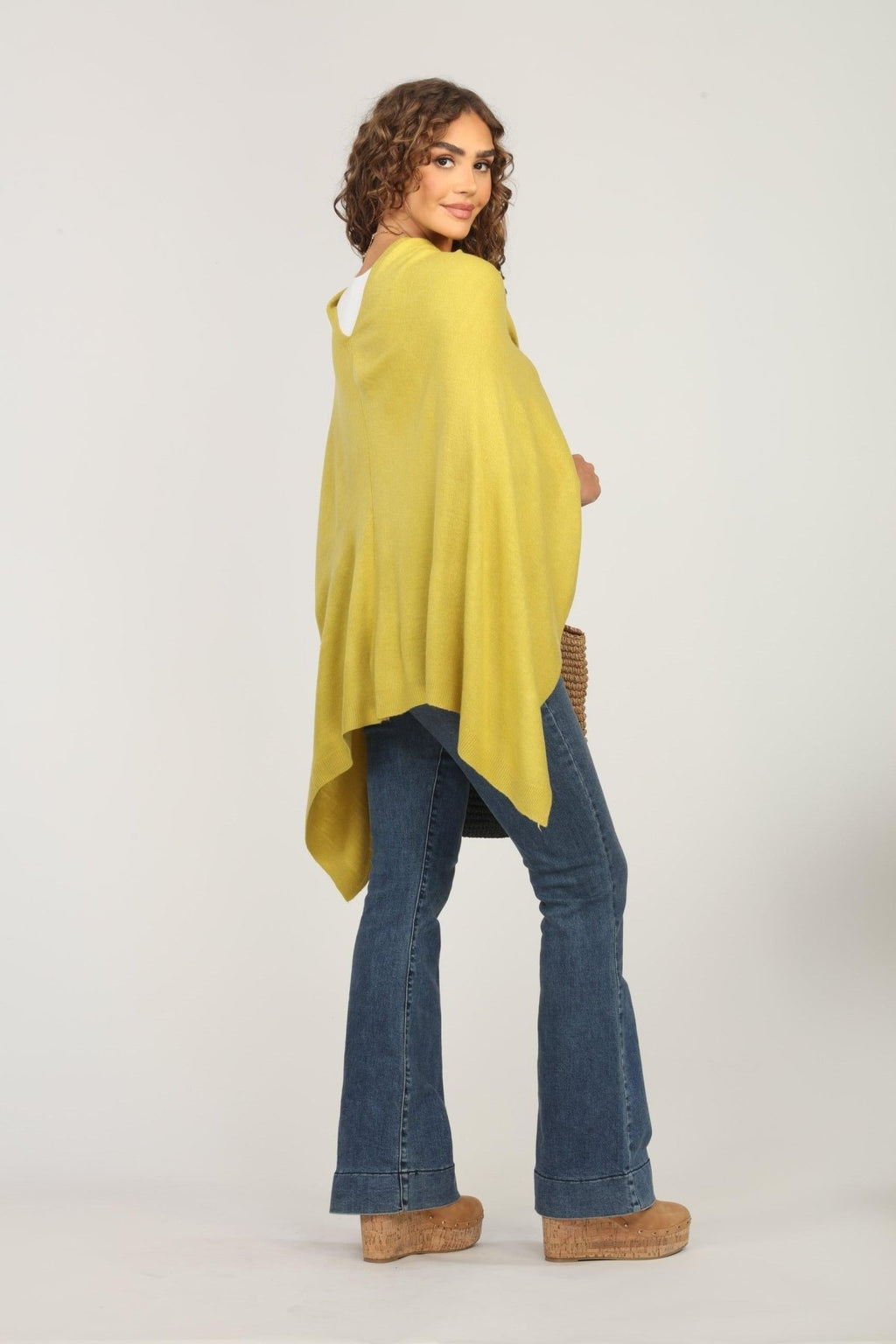 back side of lime green poncho and dark denim jeans on woman