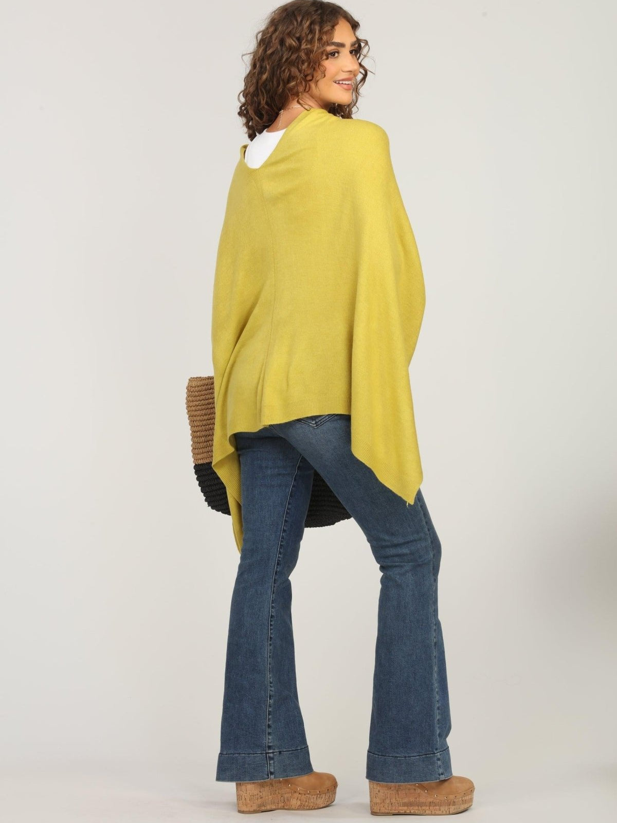 back side of lime green poncho and dark denim jeans on woman