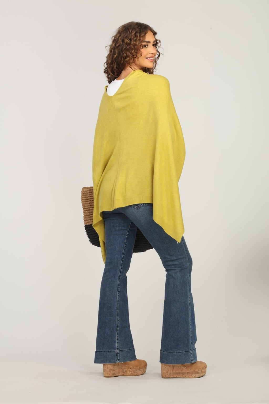 back side of lime green poncho and dark denim jeans on woman