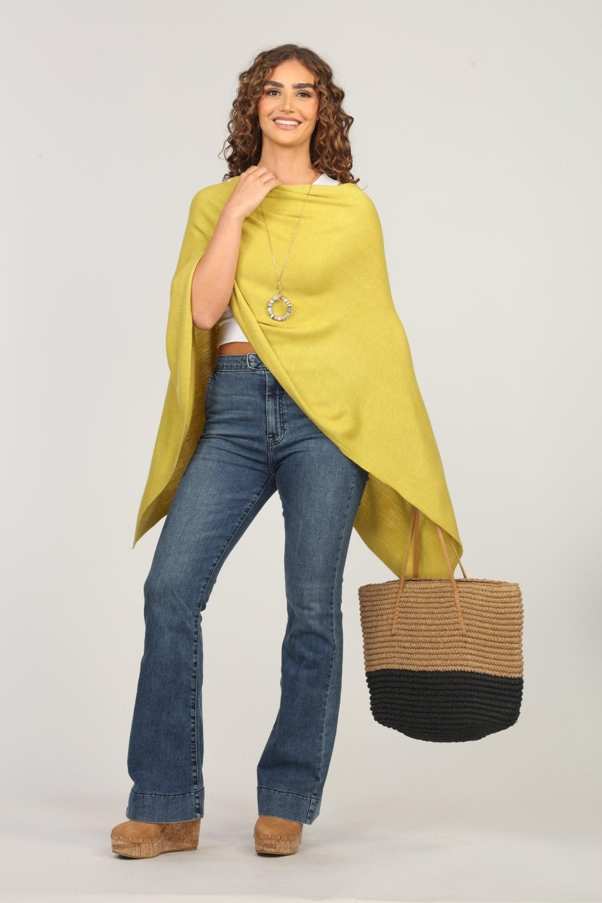 lime green poncho and dark denim jeans on woman holding woven tote bag